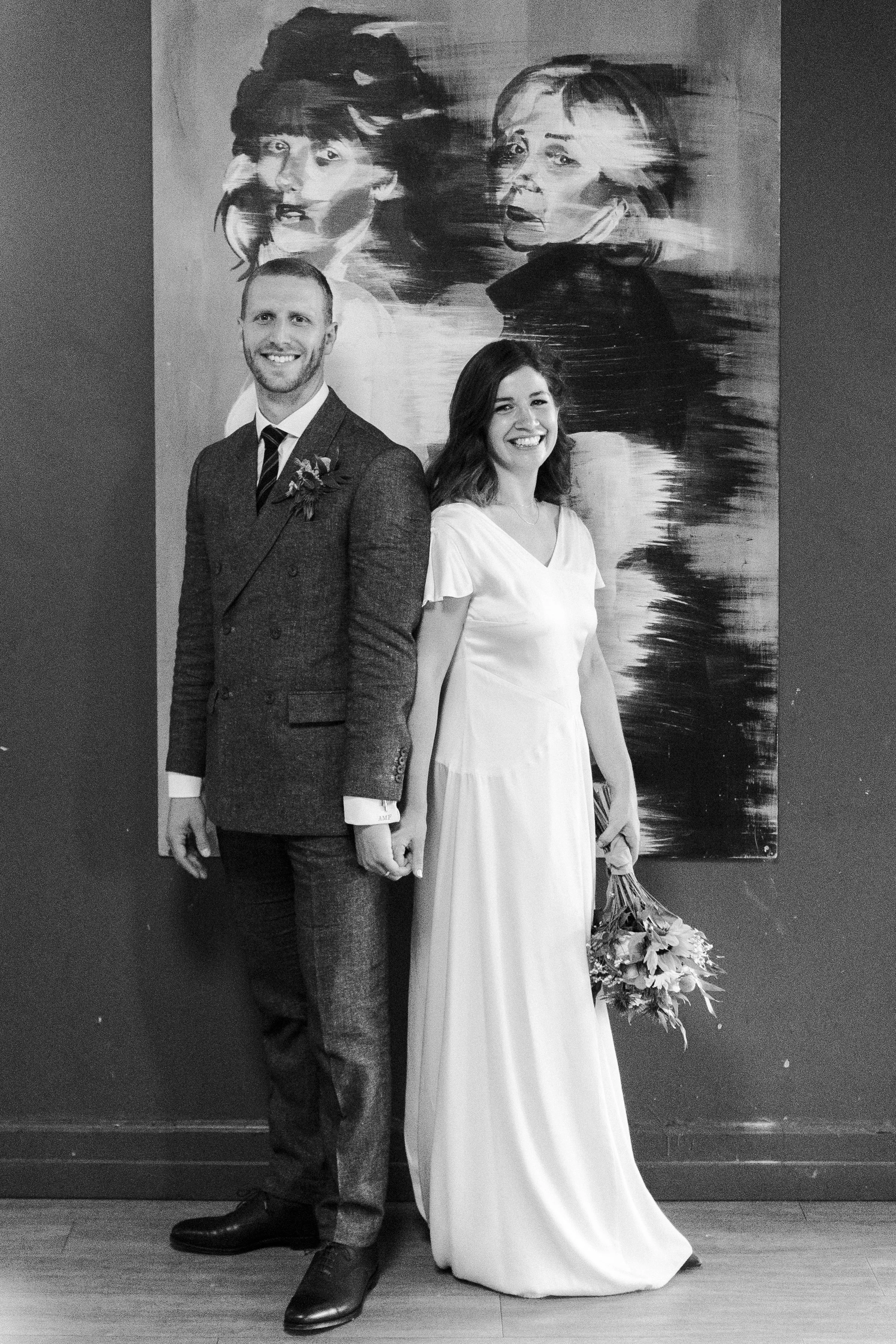 Wedding couple posing in Highgate School in front of large artwork slightly back to back at a Highgate, London Wedding.