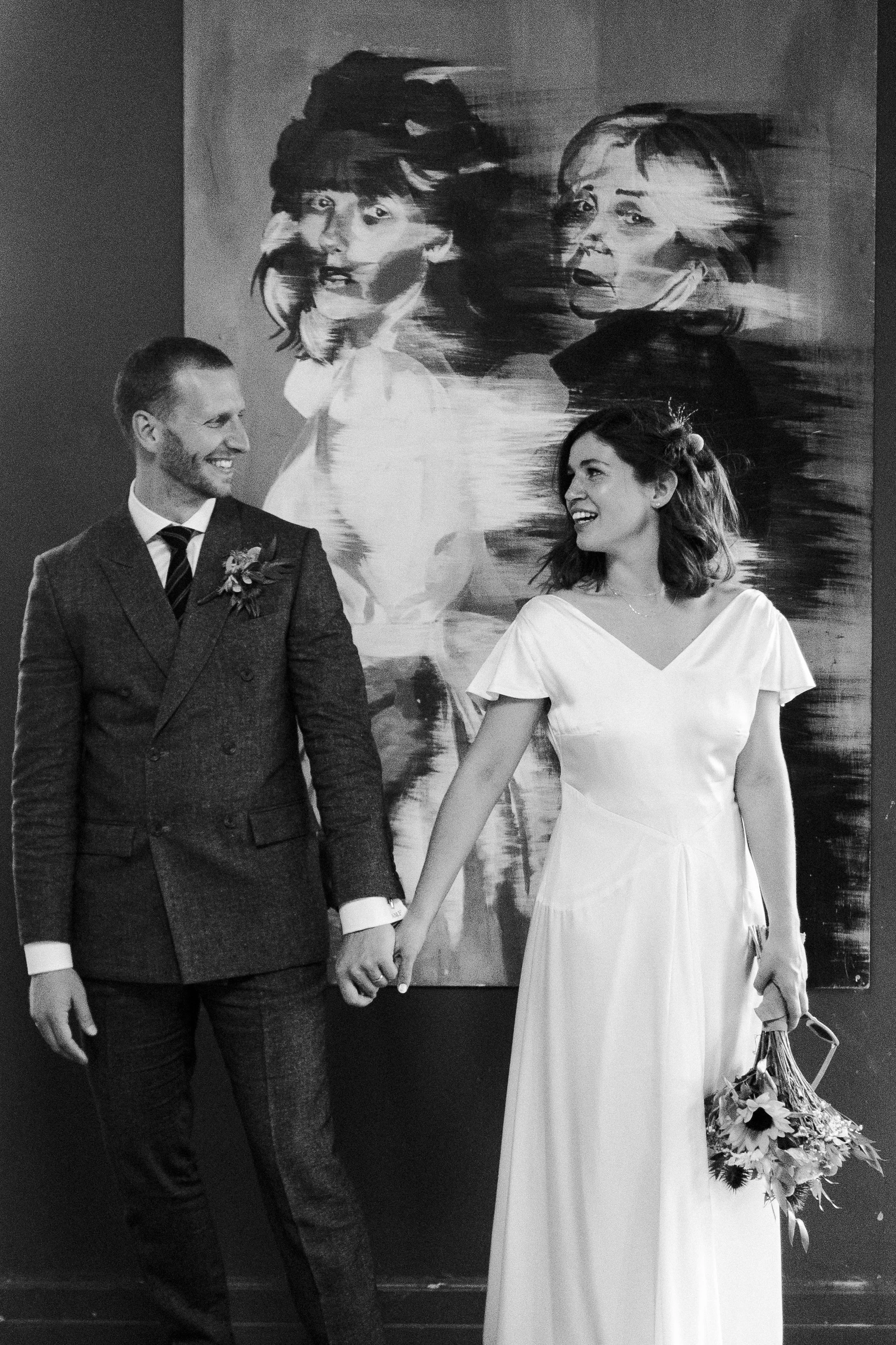 Wedding couple posing in Highgate School in front of large artwork, looking and smiling at each other at a Highgate, London Wedding.