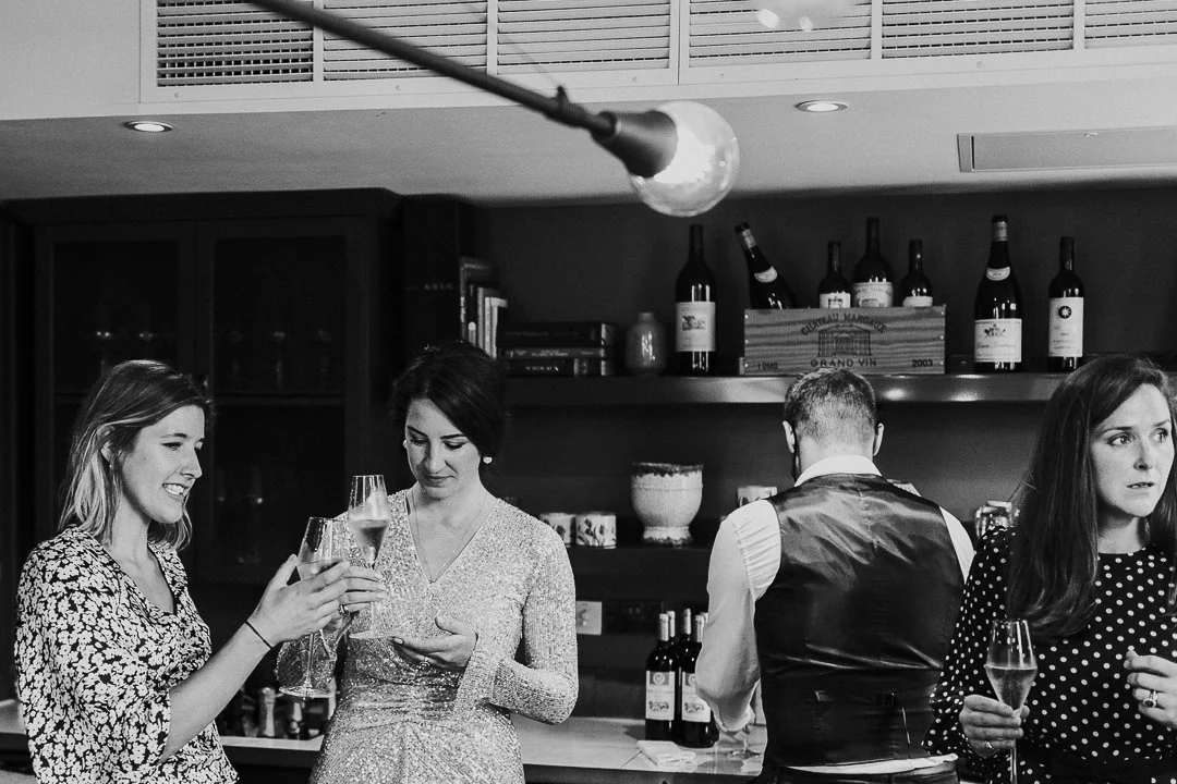 Bride & guests standing by the bar, while talking about the champagne at a restaurant at the Old Marylebone Town Hall Wedding.