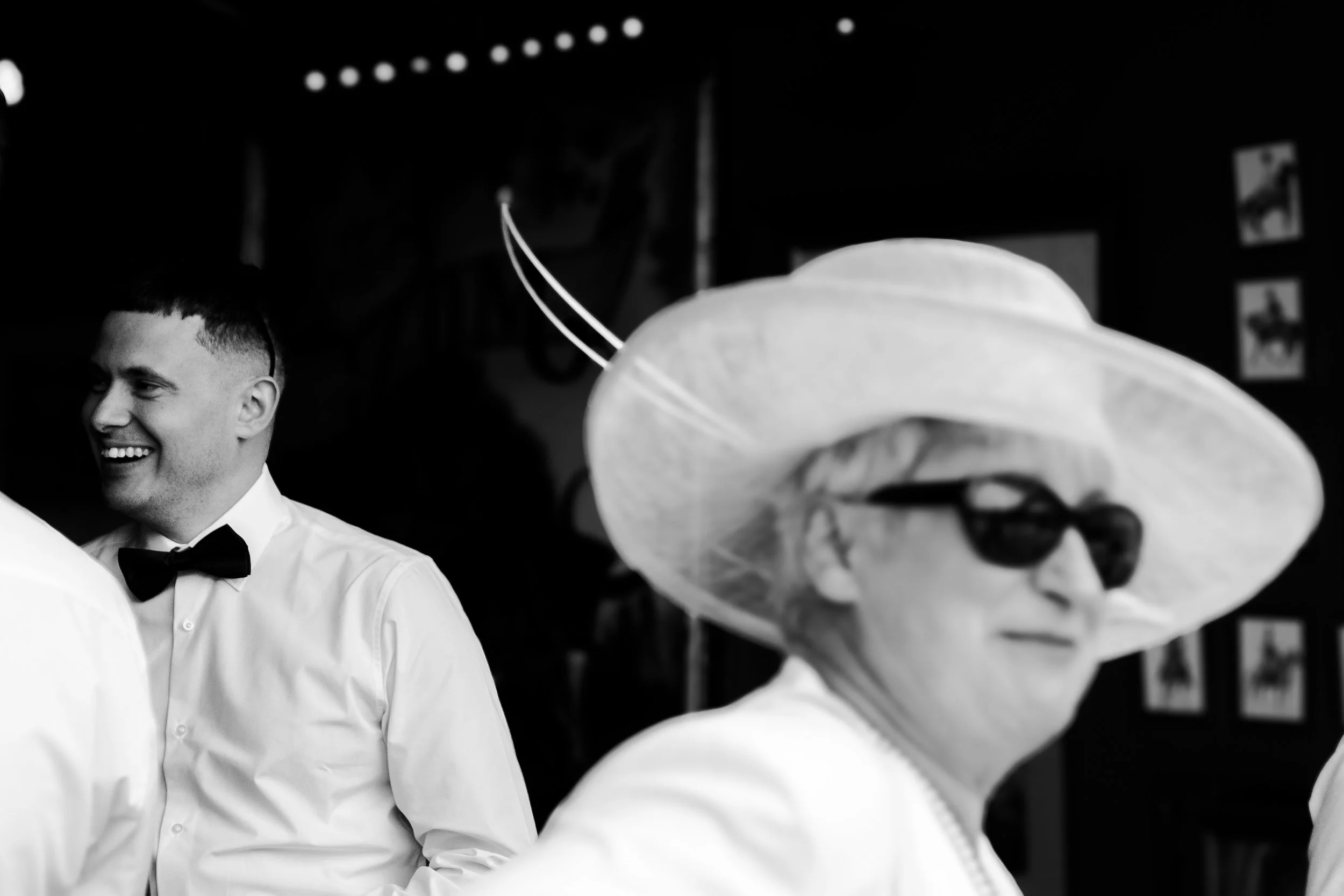 Guest with large hat walking the barn with the groom in the background laughing at a rhyse farm wedding