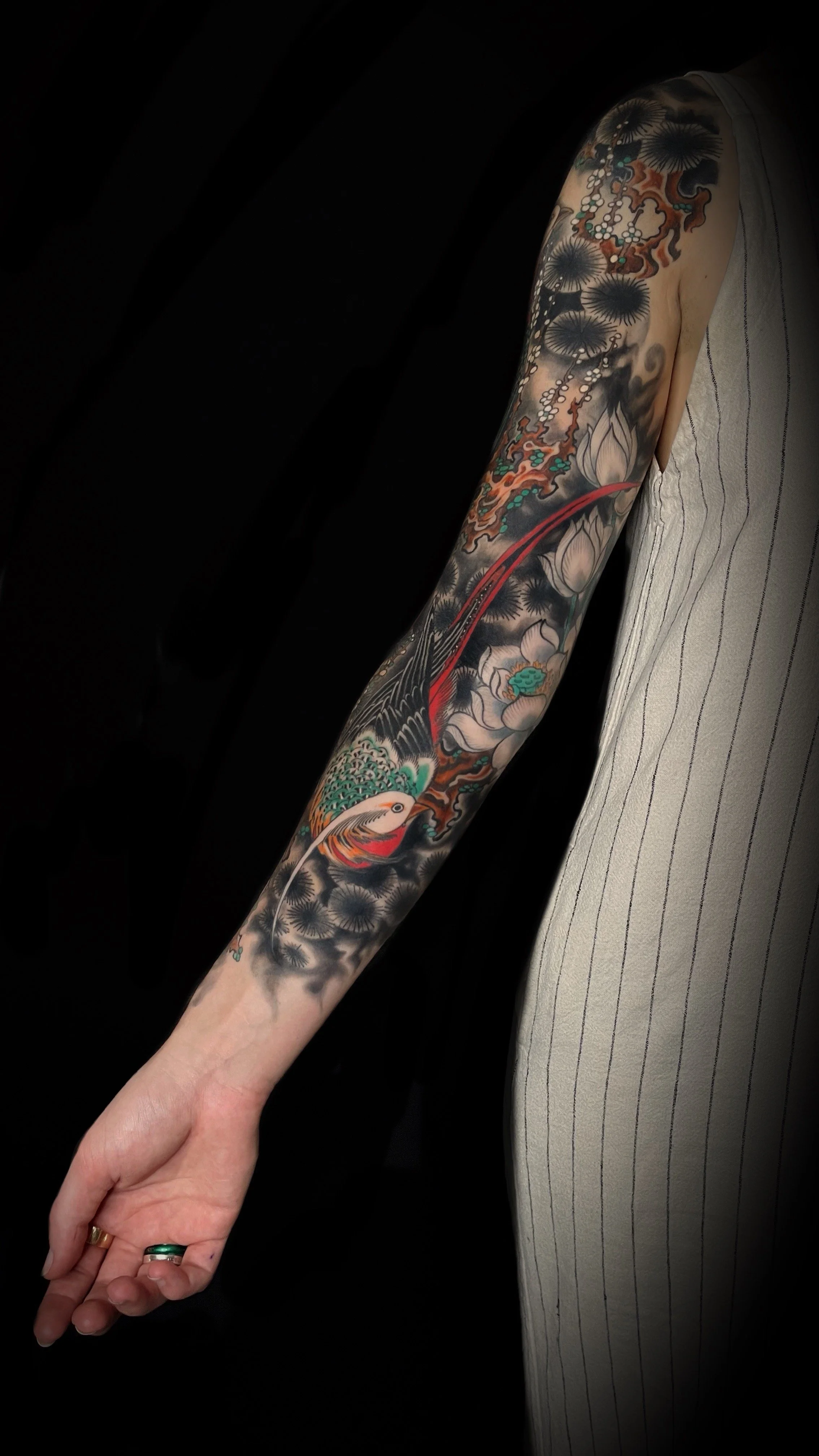 Person with detailed sleeve tattoo featuring floral and bird designs on their arm, wearing a white striped garment.
