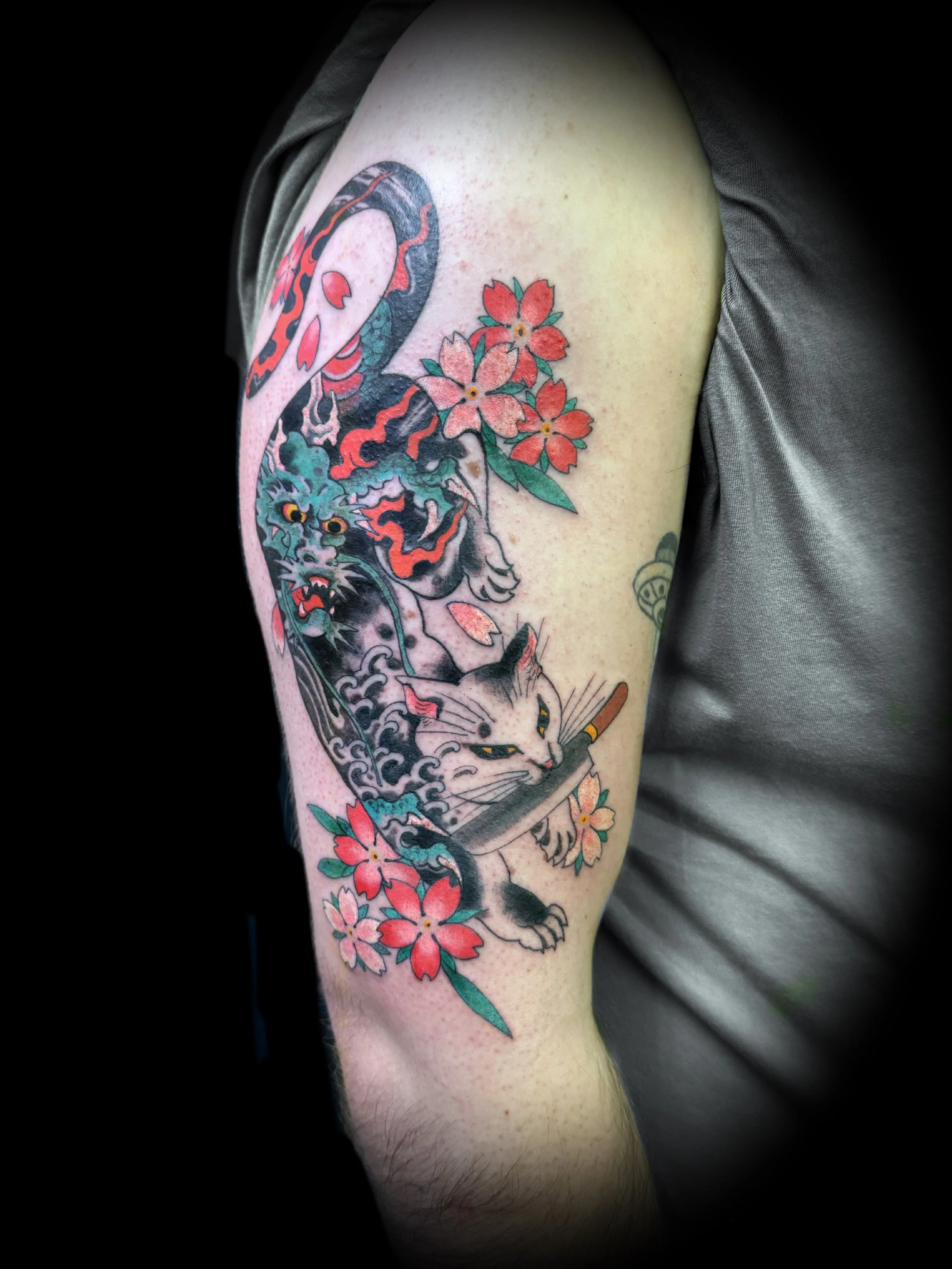 Tattoo featuring a stylized cat holding a knife with floral accents and swirling patterns on an arm.