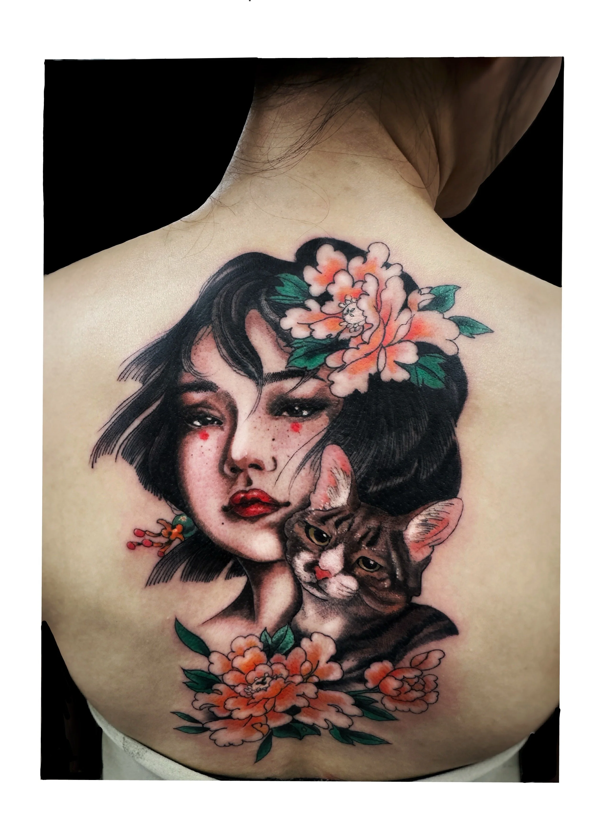 Tattoo of a woman's face with black hair, adorned with flowers, and a cat close by, on a person's back.
