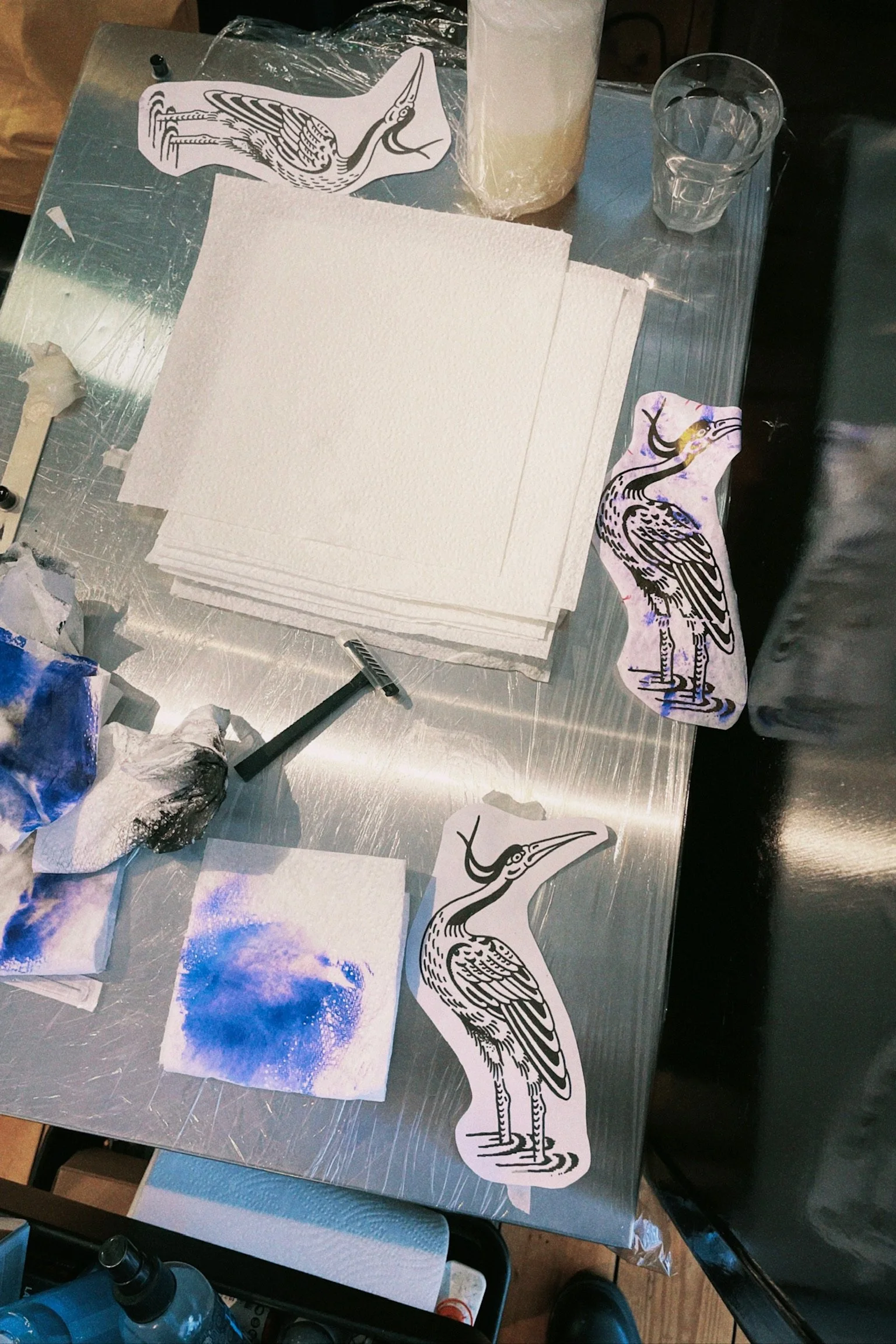 Tattoo art workstation with heron designs, paper towels, ink stains, and tools.