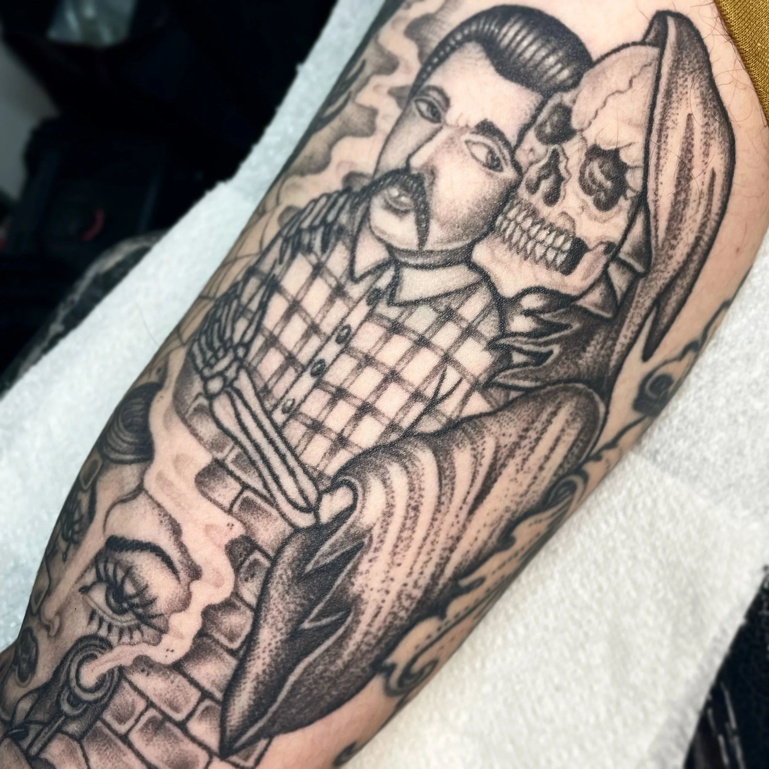 Tattoo of a skeletal figure with a man in a checkered shirt, surrounded by surreal elements.