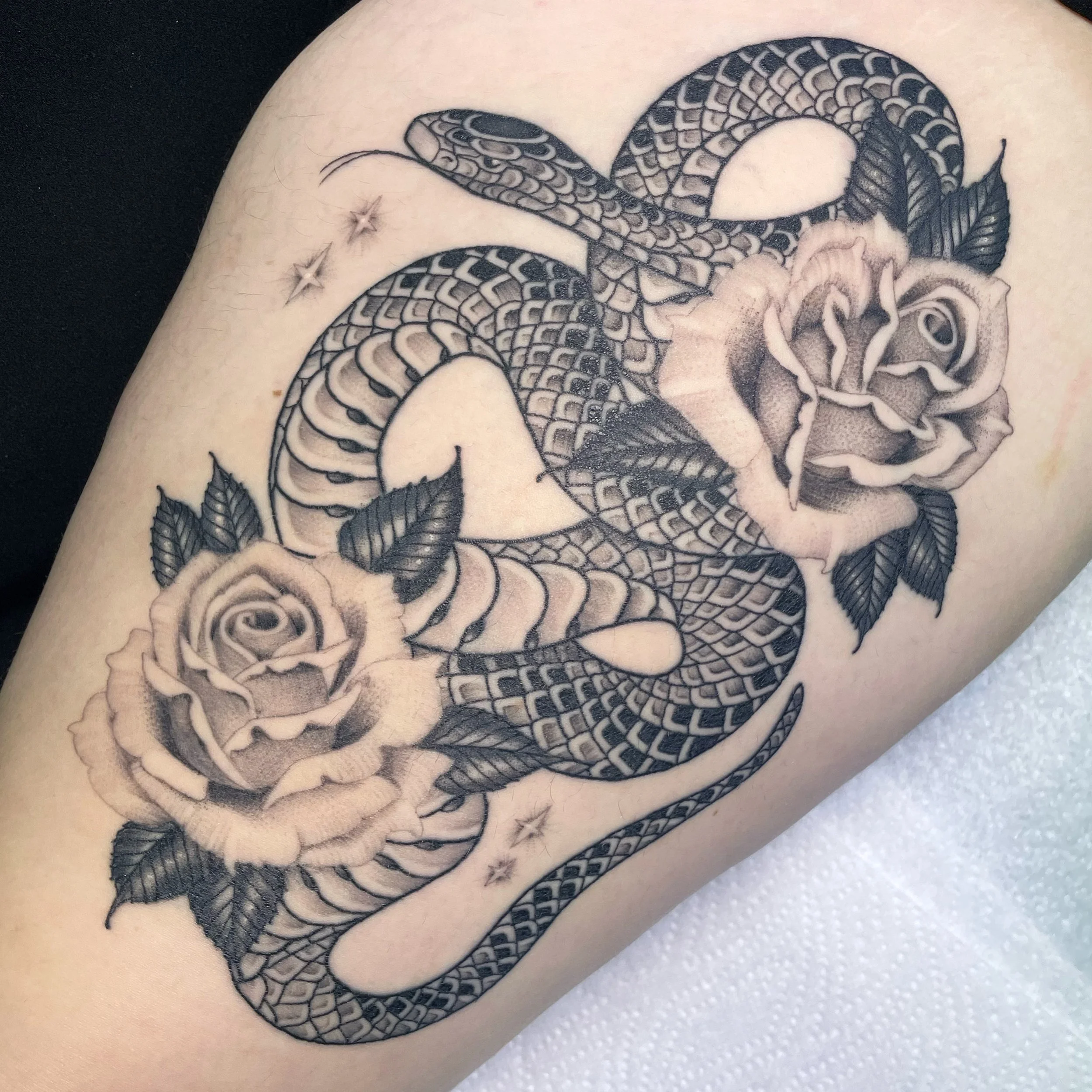 Tattoo of a coiled snake intertwined with roses on skin, featuring intricate shading and details.