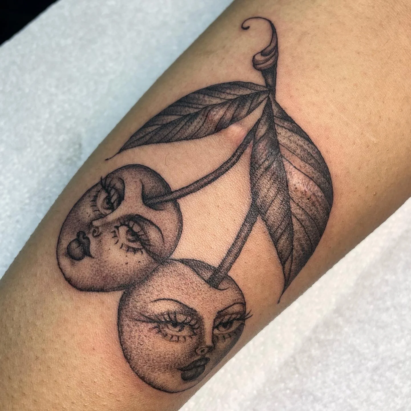 Tattoo of cherries with human faces and leaves on skin