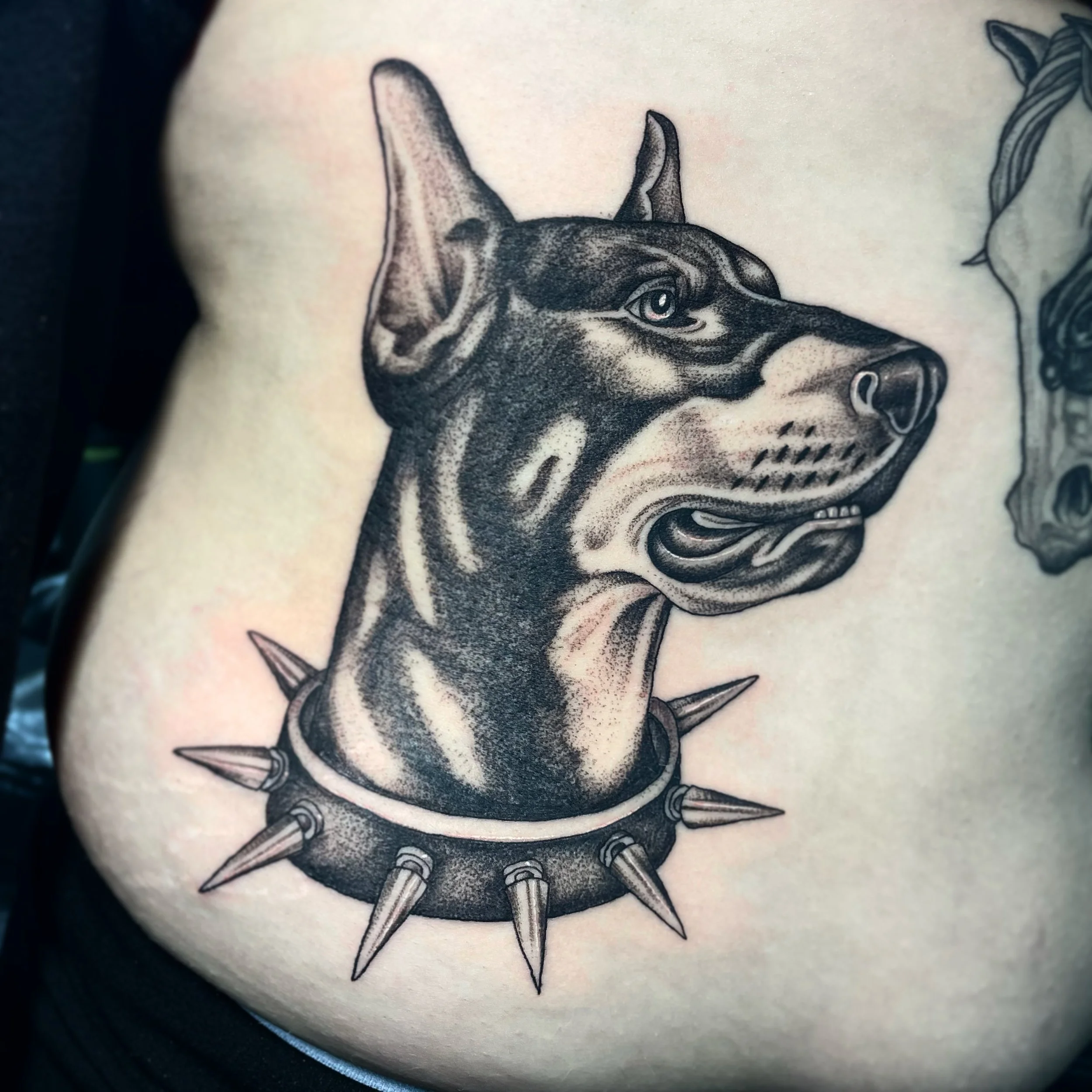 Tattoo of a dog's head with a spiked collar on skin