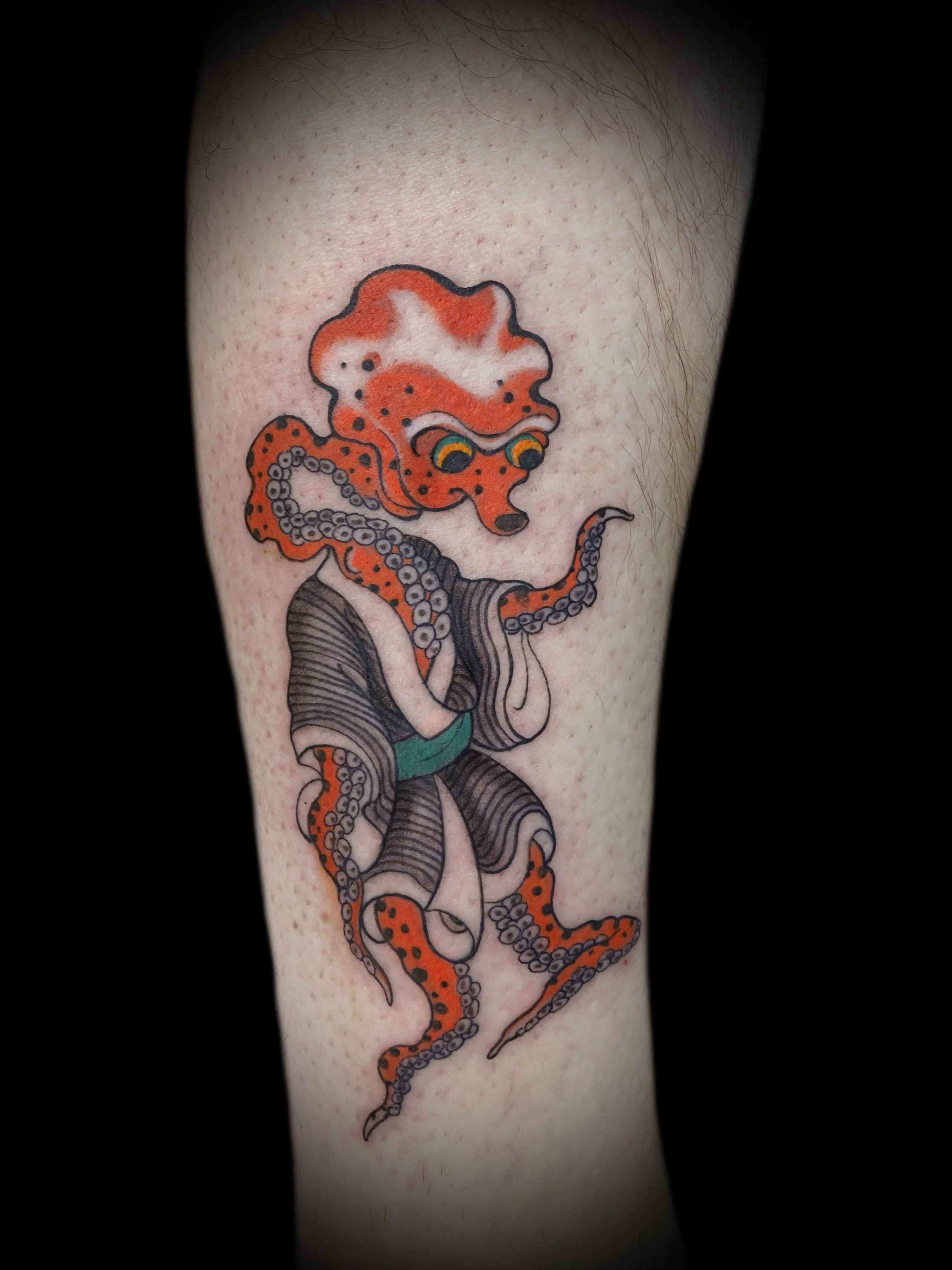 Tattoo of an anthropomorphic orange octopus wearing traditional Japanese clothing on a person's skin.