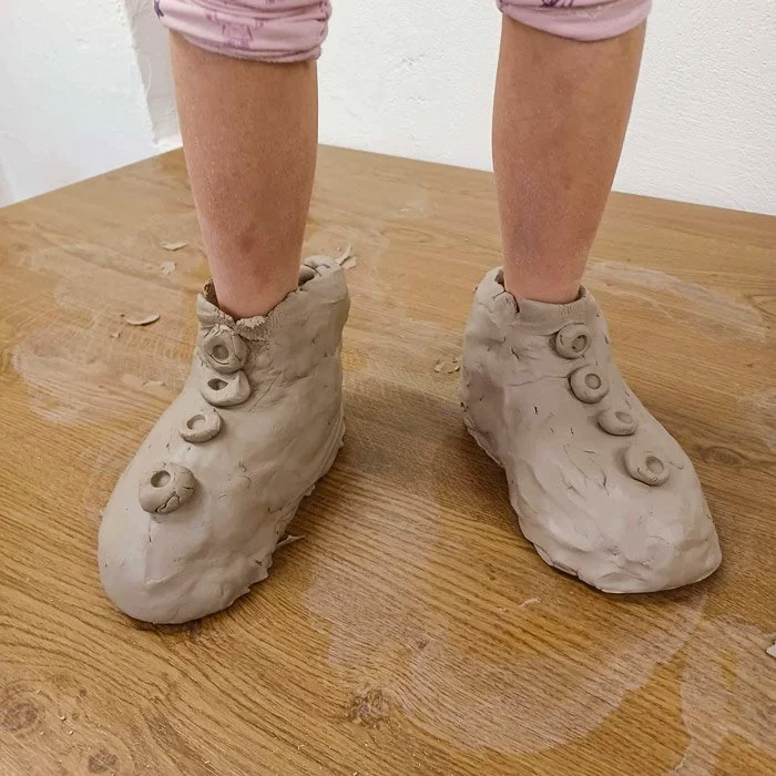 Kind trägt selbst gefertigte Tonstiefel mit Knopfverzierungen auf einem Holzboden.
