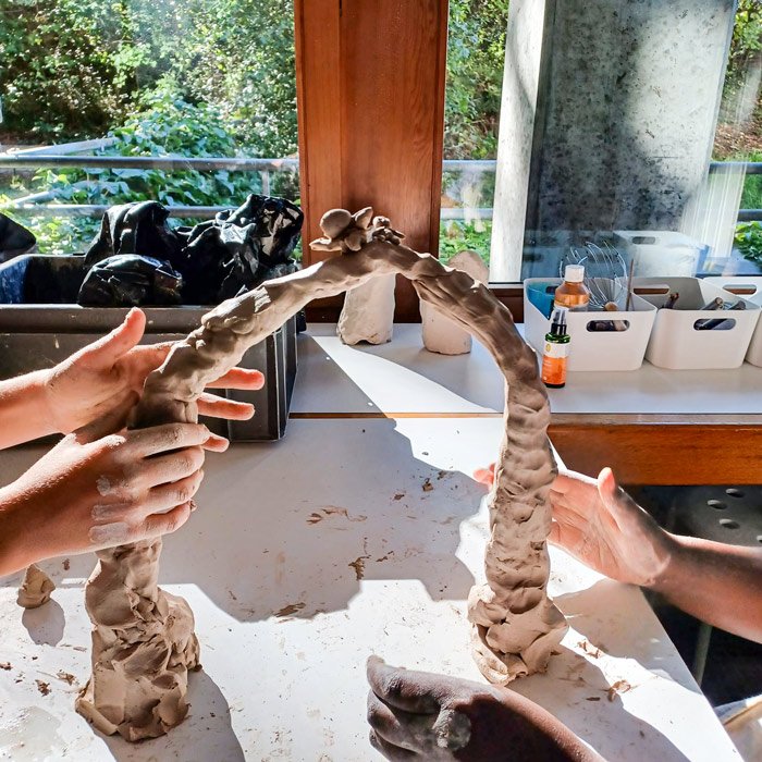 Hände formen eine große Tonplastik mit bogenförmiger Struktur auf einem Arbeitstisch