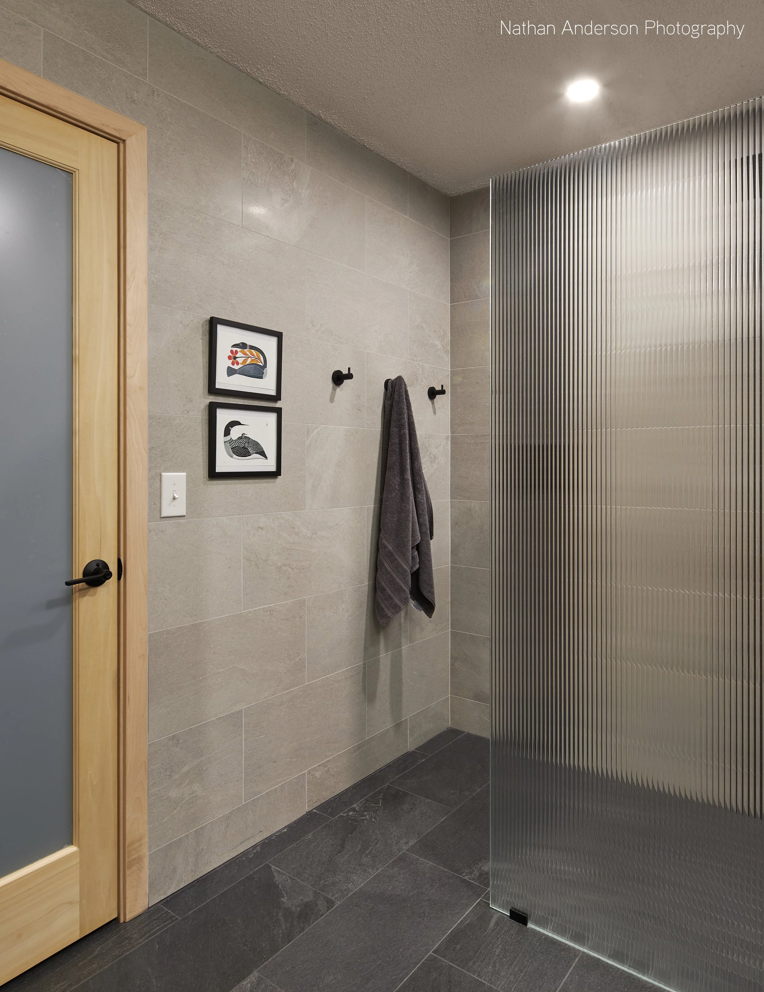 This zero-entry shower replaced a fiberglass shower and bathtub. Now, reeded glass, handcrafted maple doors , and ample space provide comfort and convenience. All tile shown is Red List Free.
