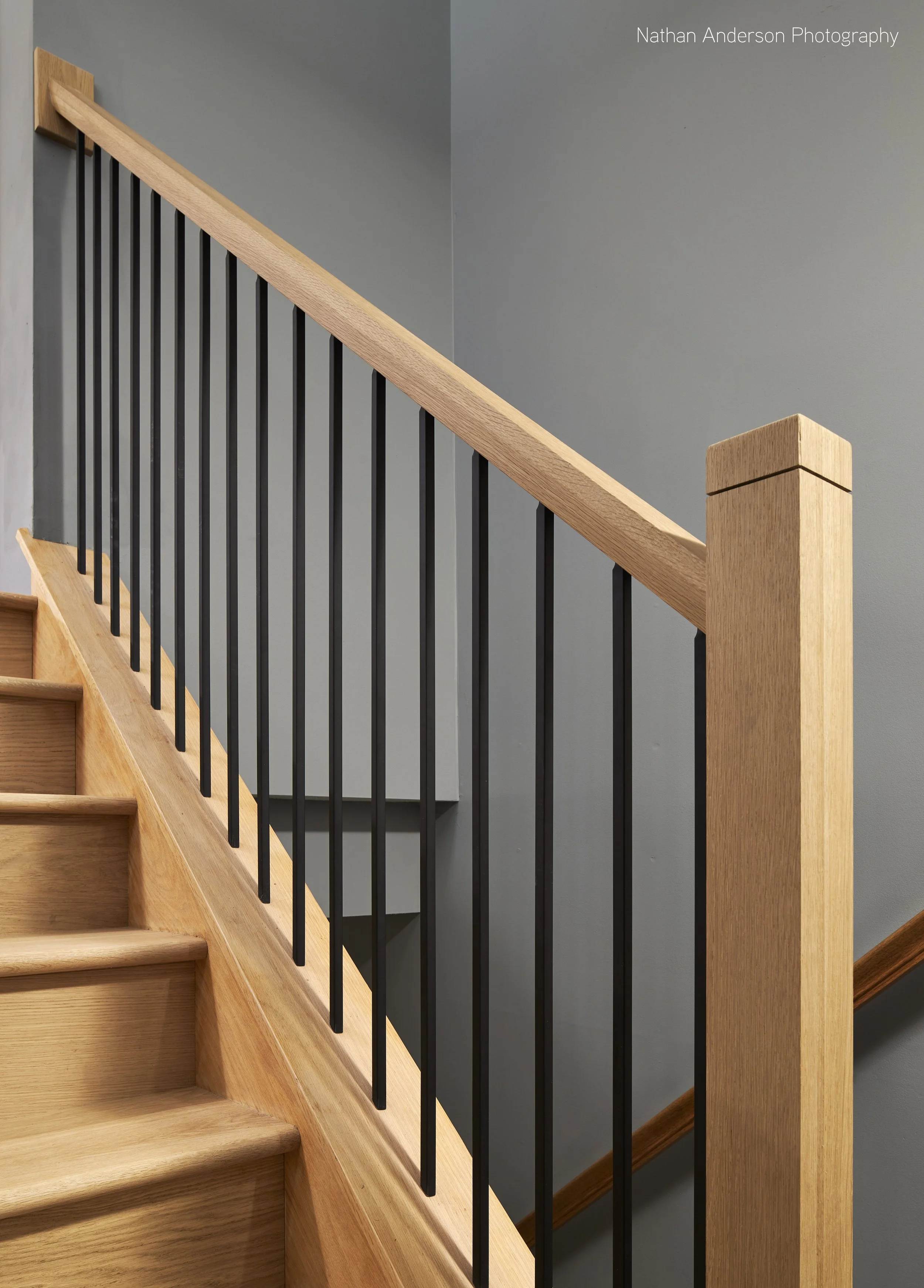 The previous honey Oak, traditional railing was replaced with this custom designed White Oak railing. The existing structure and stair skirt were meticulously sanded and matched to the new railing; the aluminum balusters were precisely aligned, with 
