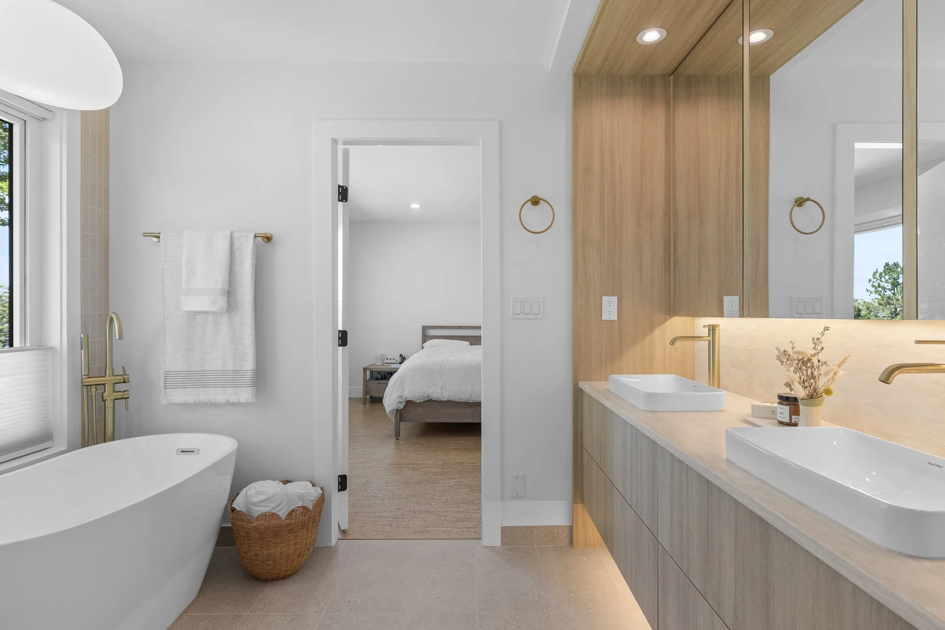 Modern bathroom with white walls, a bathtub, a large window, a towel rack, and a double sink vanity with wood cabinetry and mirrors.