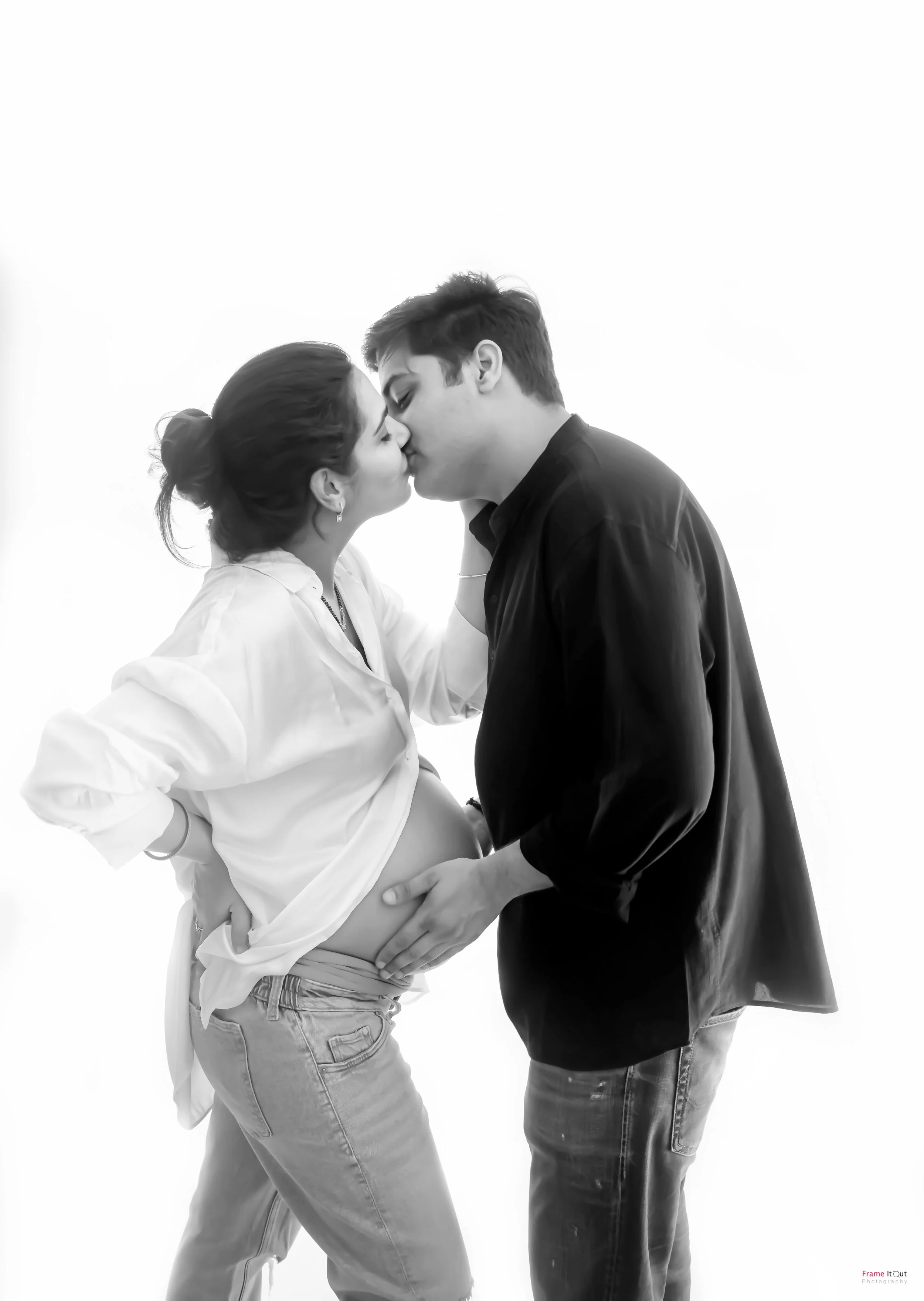 Black and white maternity photo of expecting couple sharing a gentle kiss in studio