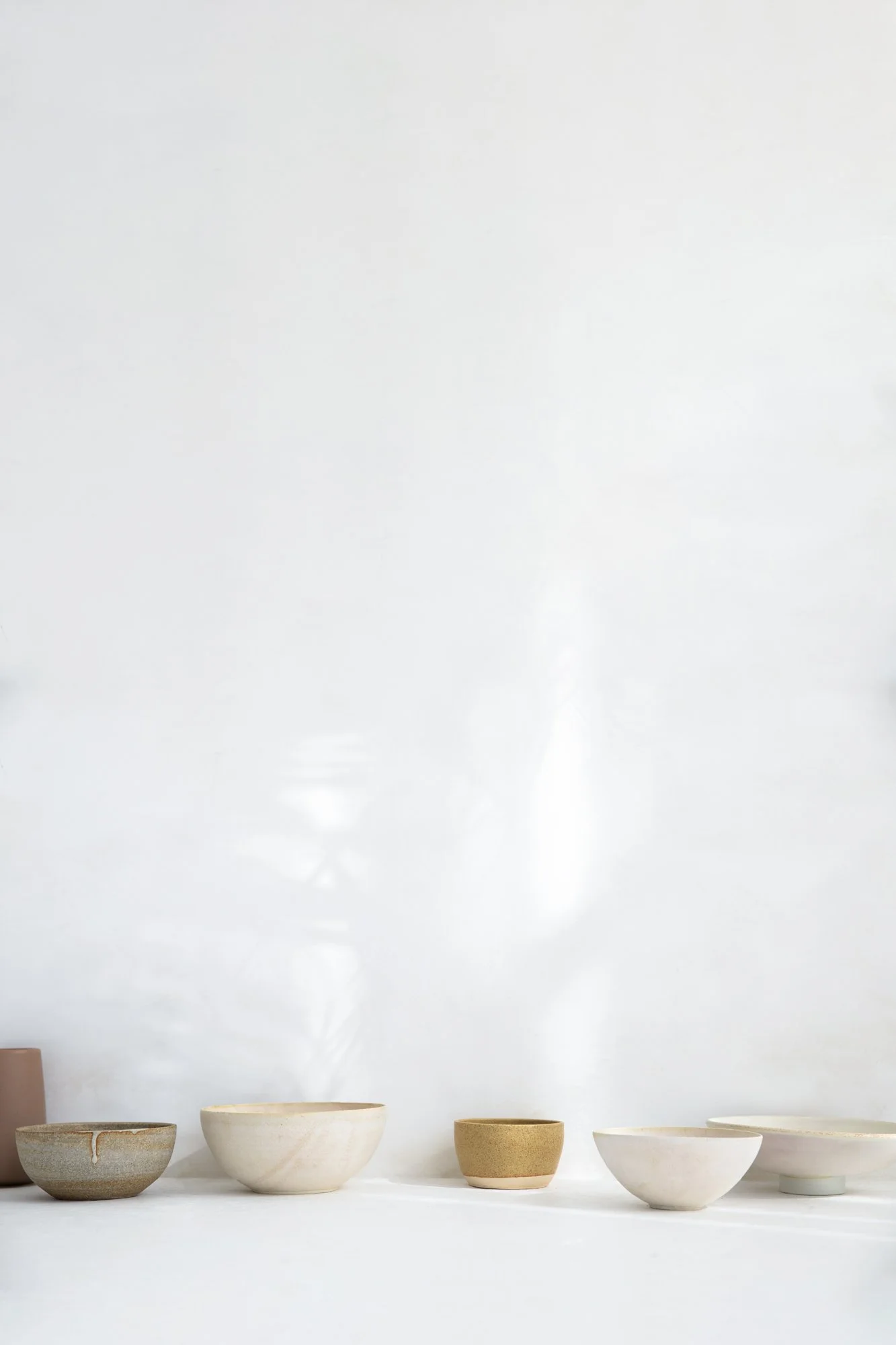 Collection of various pottery bowls and cups on a white surface with a white wall background. prop rental