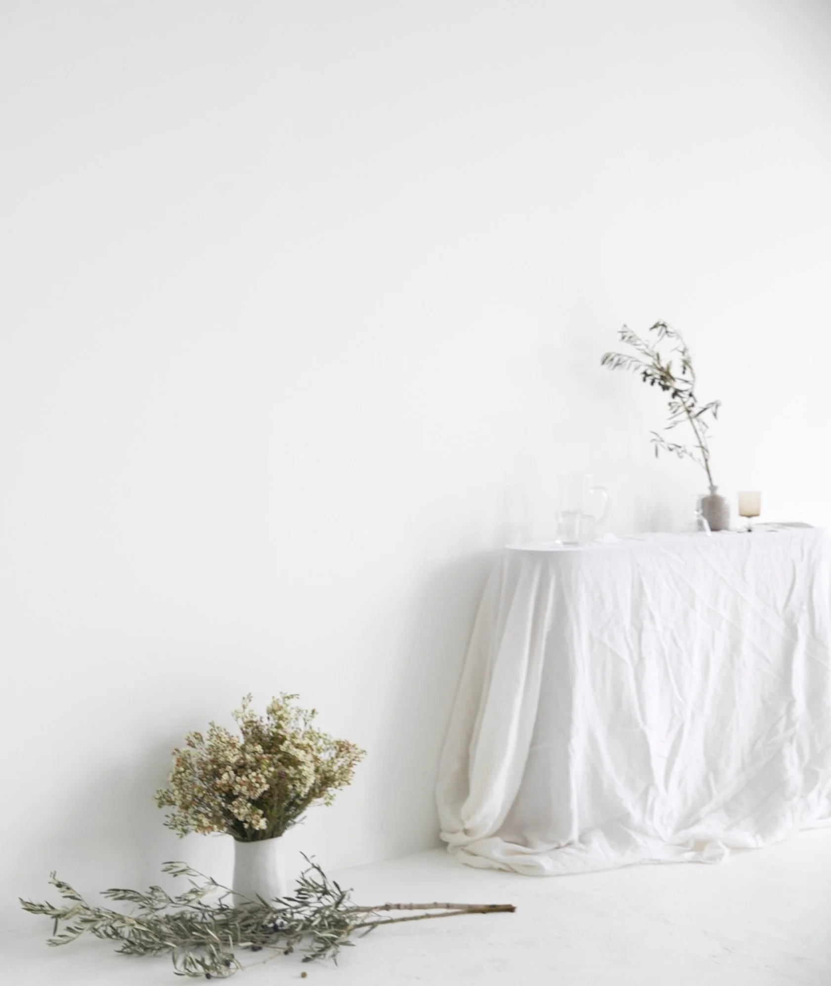 A table covered with a white tablecloth, with a large vase of flowers, and a candles in a jar on the right side, set against a plain white background. workshop space