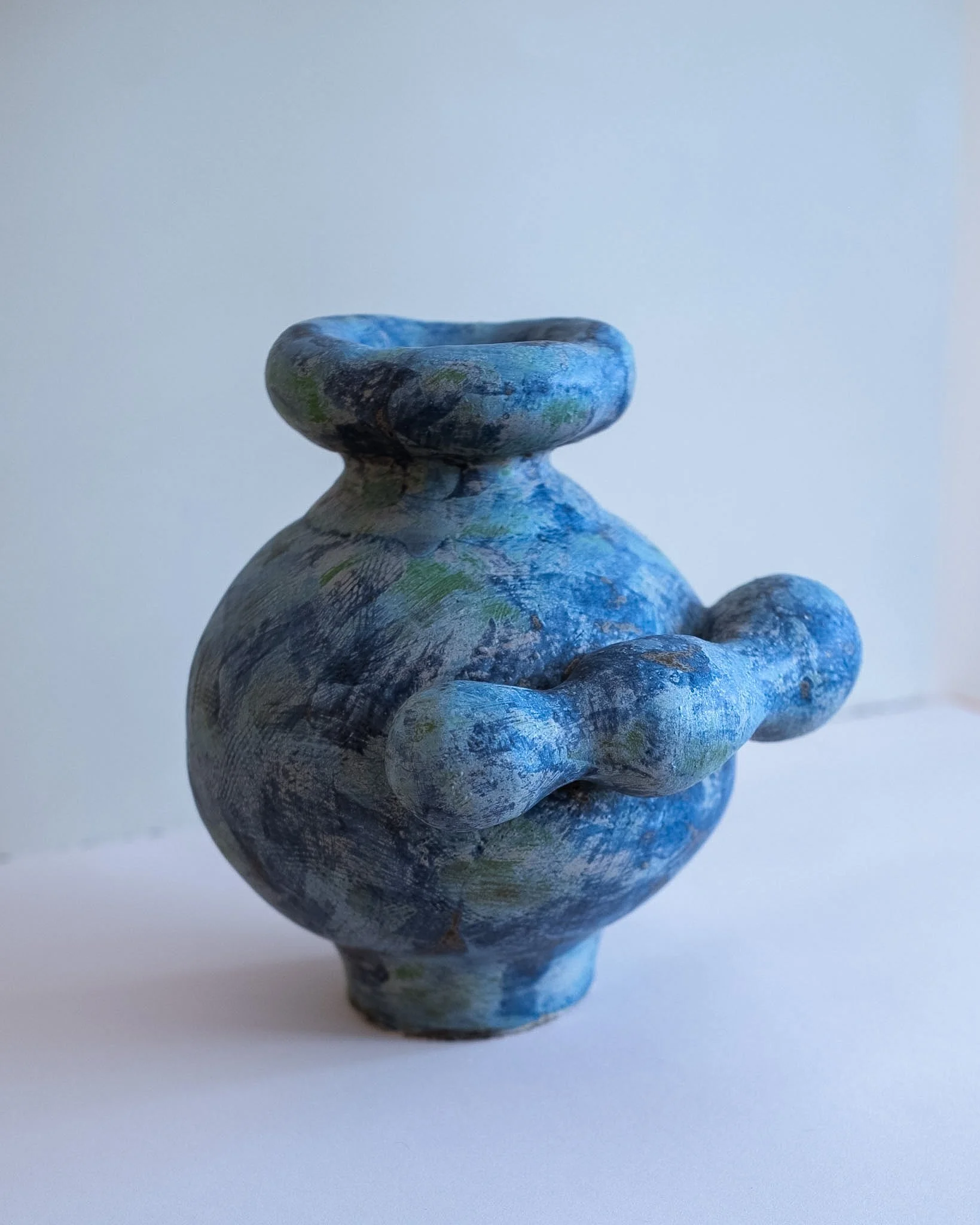 Close-up of a small, colorful, hand-painted ceramic vase with a wide opening against a plain background.