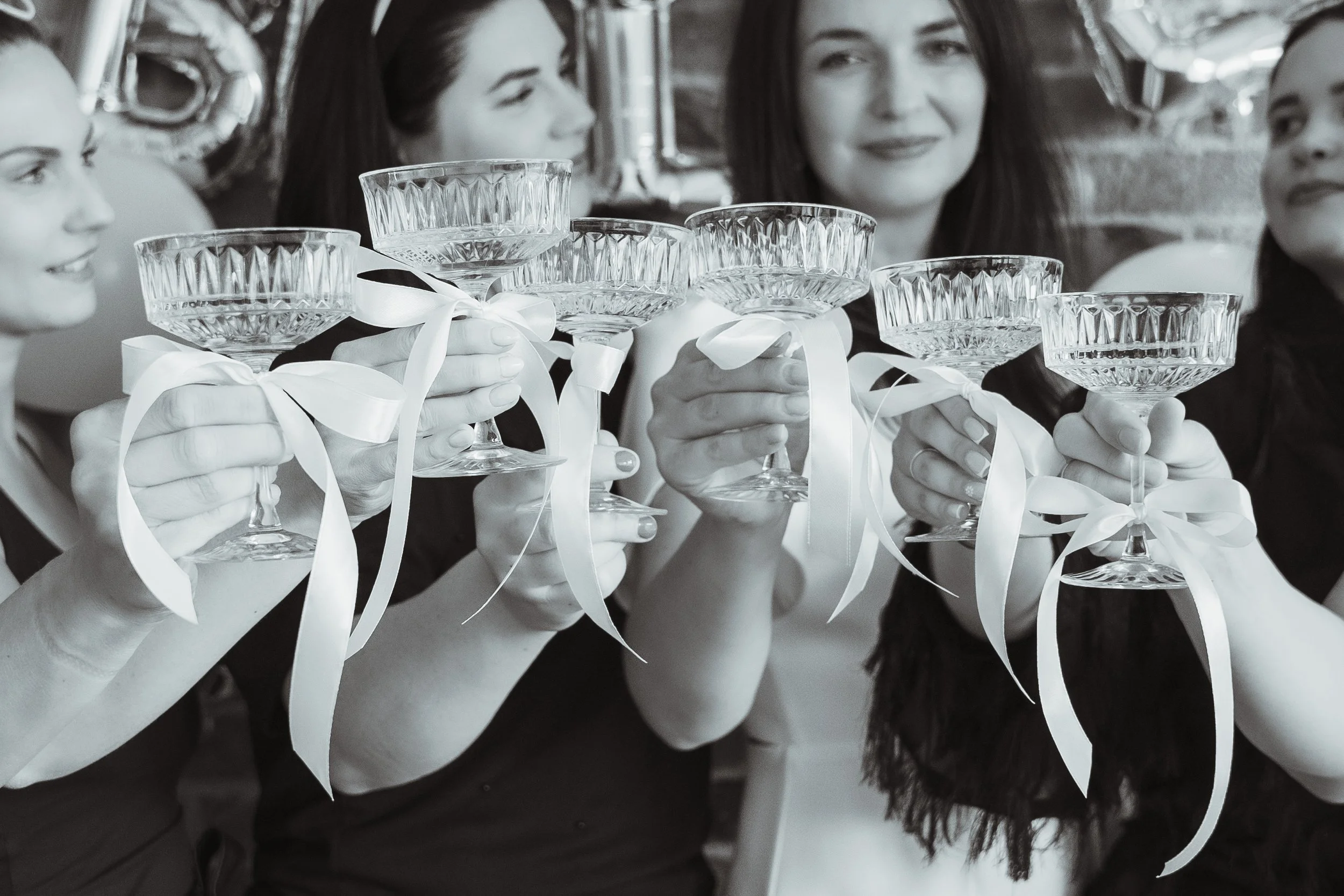 Women holding crystal glasses with ribbons, celebrating at a party.