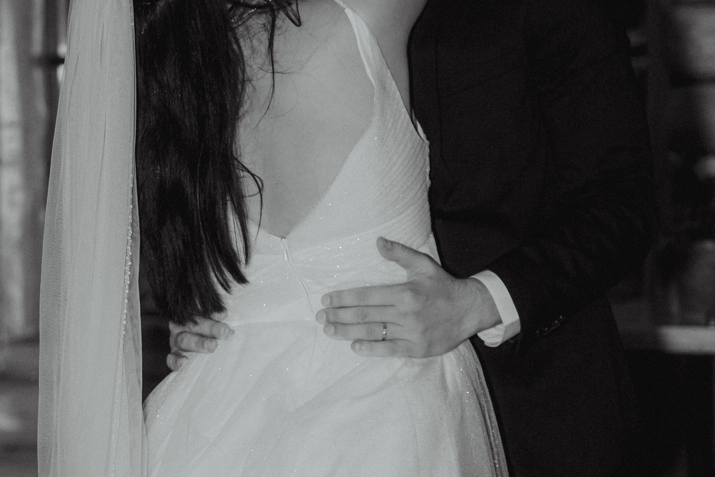Close-up of a bride and groom embracing, focusing on the bride's white wedding gown and the groom's black suit.