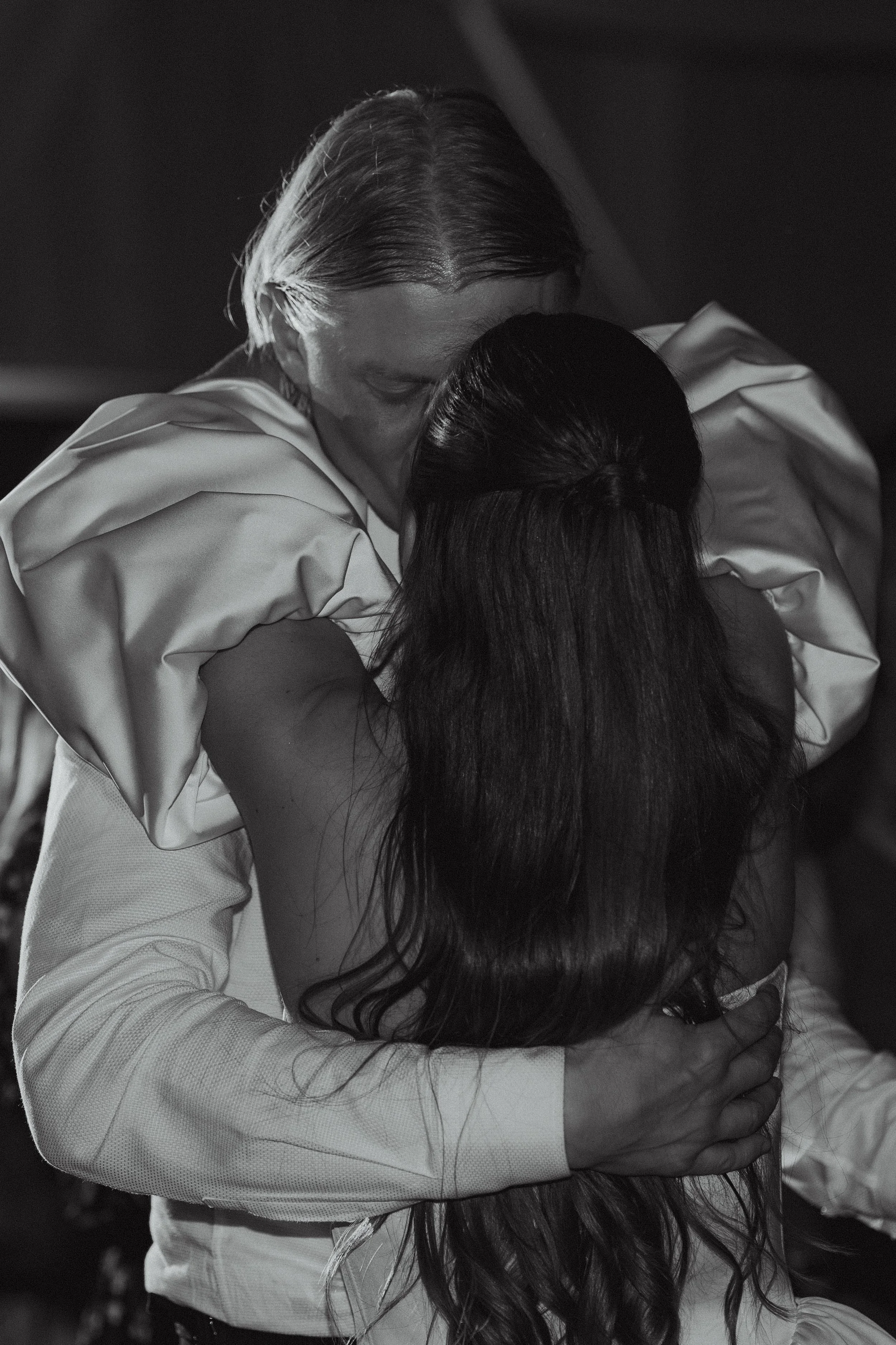 A person with long hair embracing another person, both shown in black and white, with the second person's face partially visible.