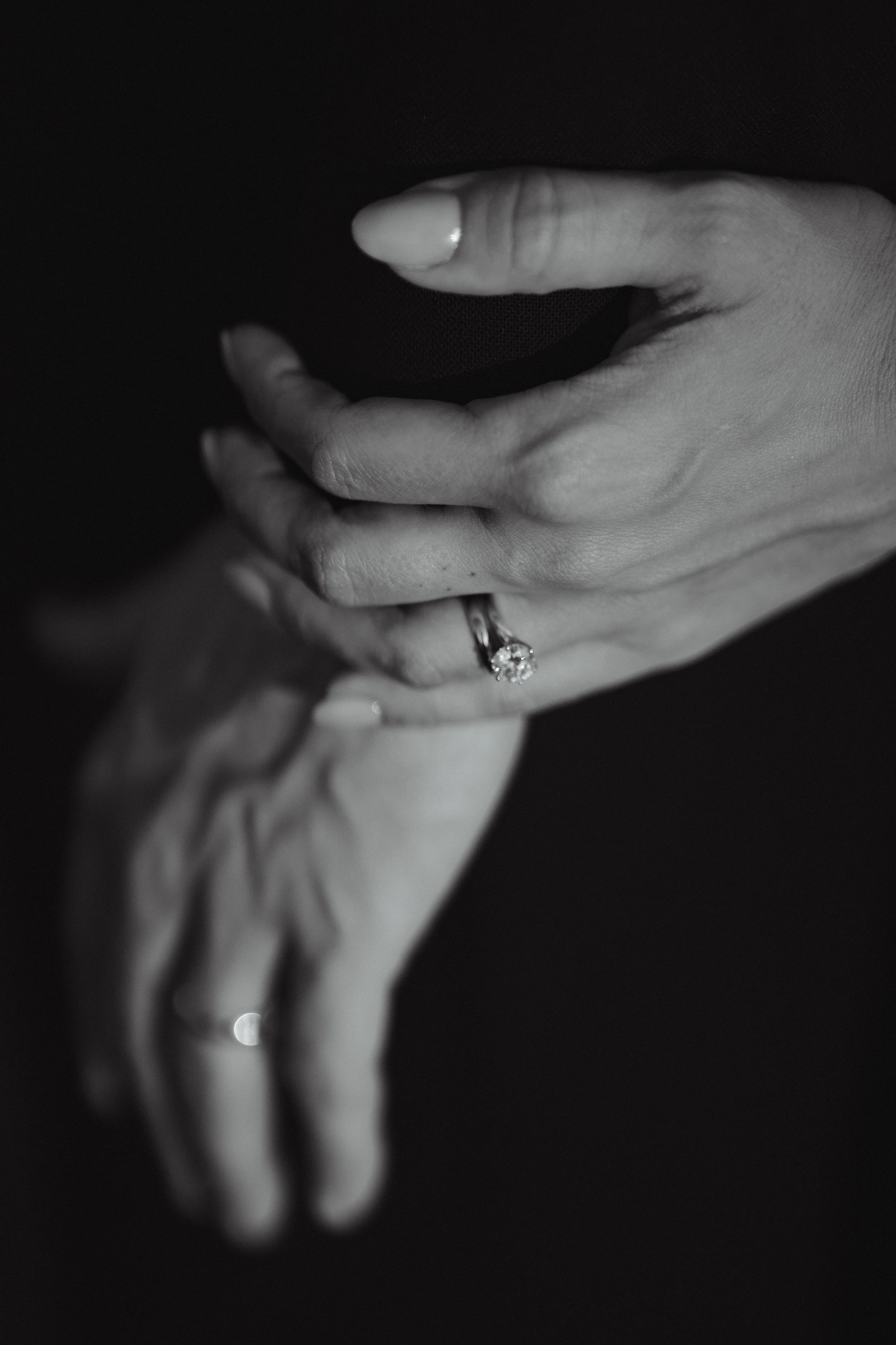 Close-up of two hands, one with an engagement ring, against a dark background