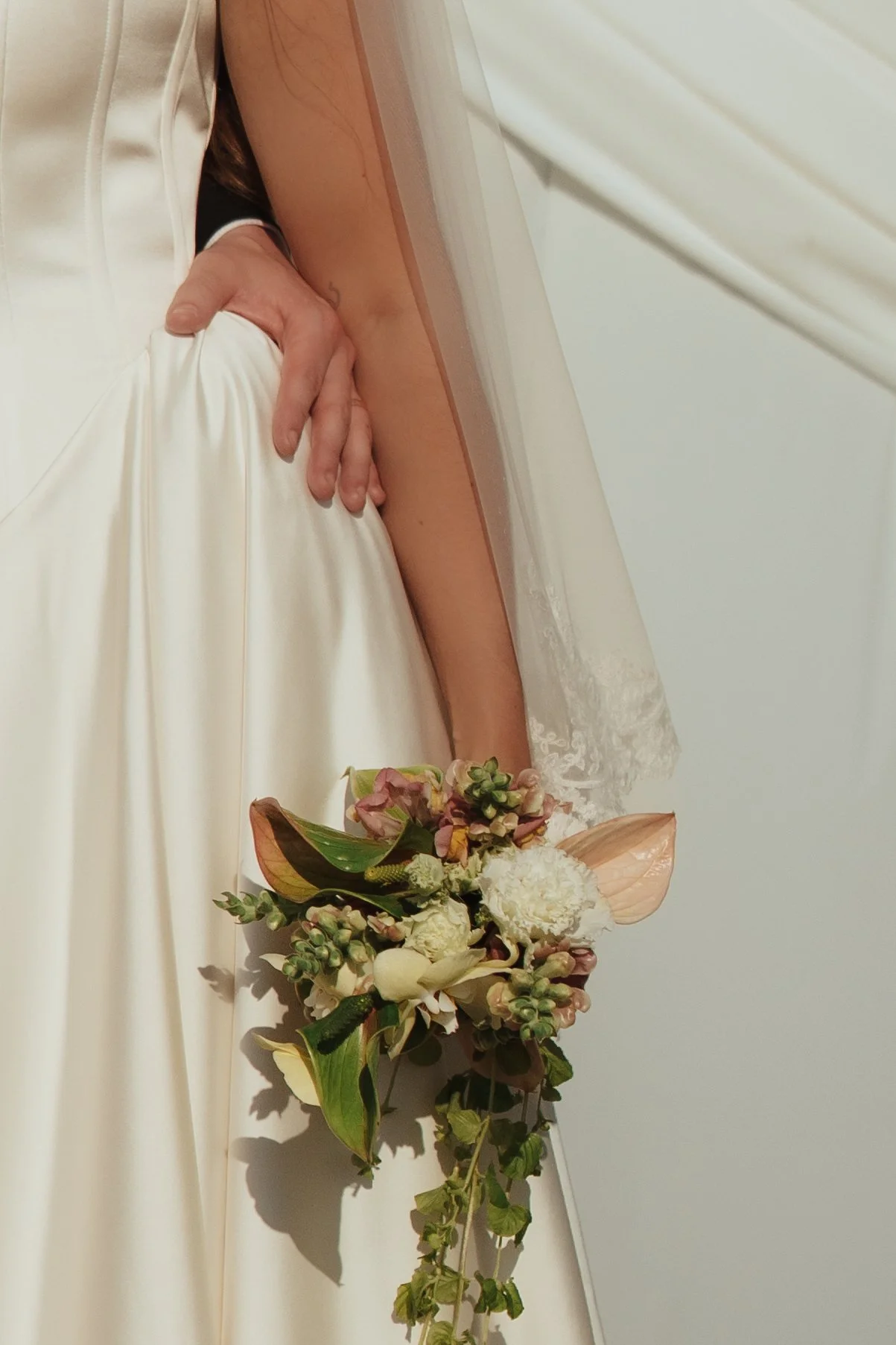 Close-up of a bride holding a cascading bouquet of flowers, with part of her wedding dress and veil visible.