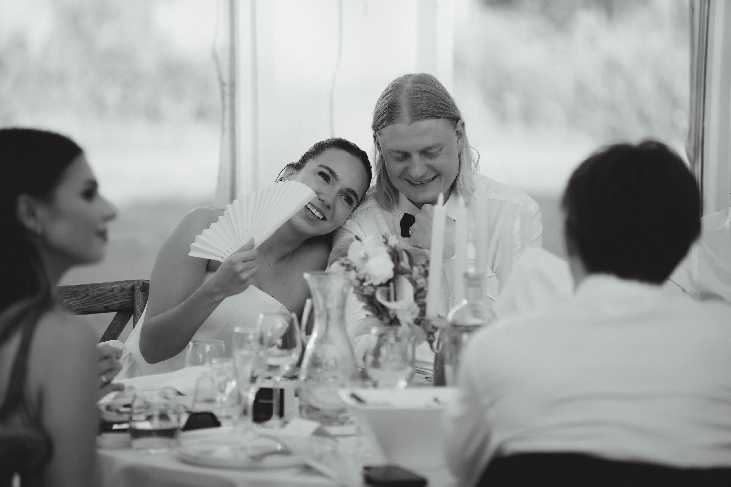 Black-and-white photo of a family gathered around a table at a celebration, with a woman holding a fan and a man smiling at her.
