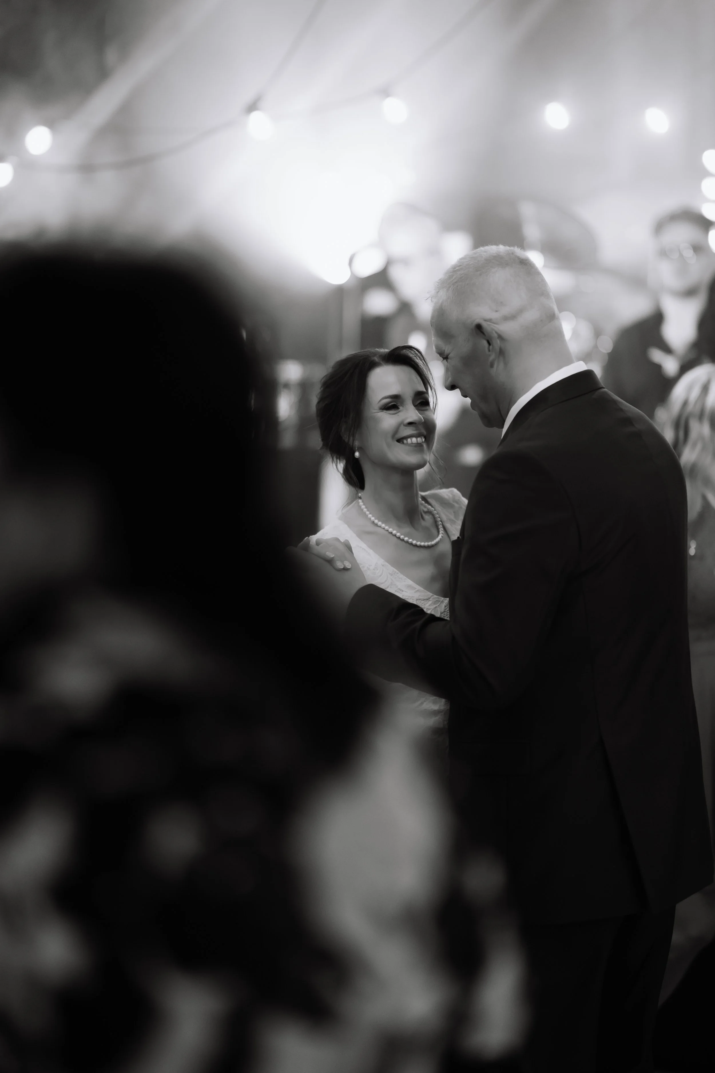 A black and white photo of a couple dancing at a wedding reception, with the woman smiling and looking at the man.