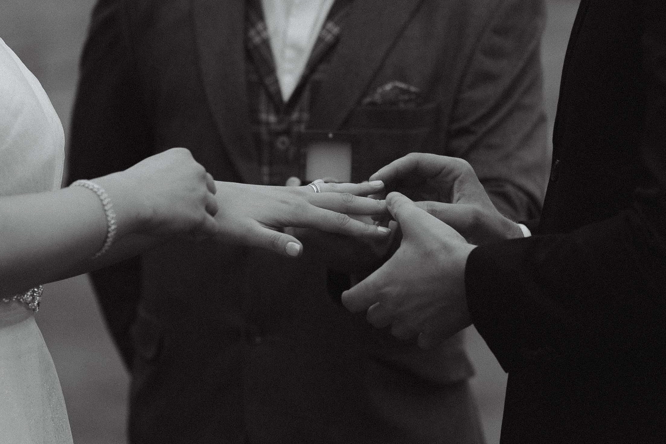 A black and white photo of a wedding ceremony showing a couple exchanging rings with an officiant.