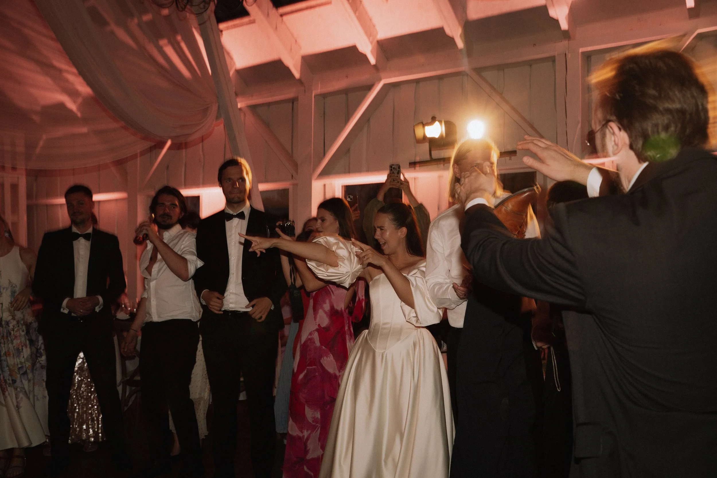 Group of people dressed in formal attire, dancing and celebrating at a wedding reception in a decorated venue.