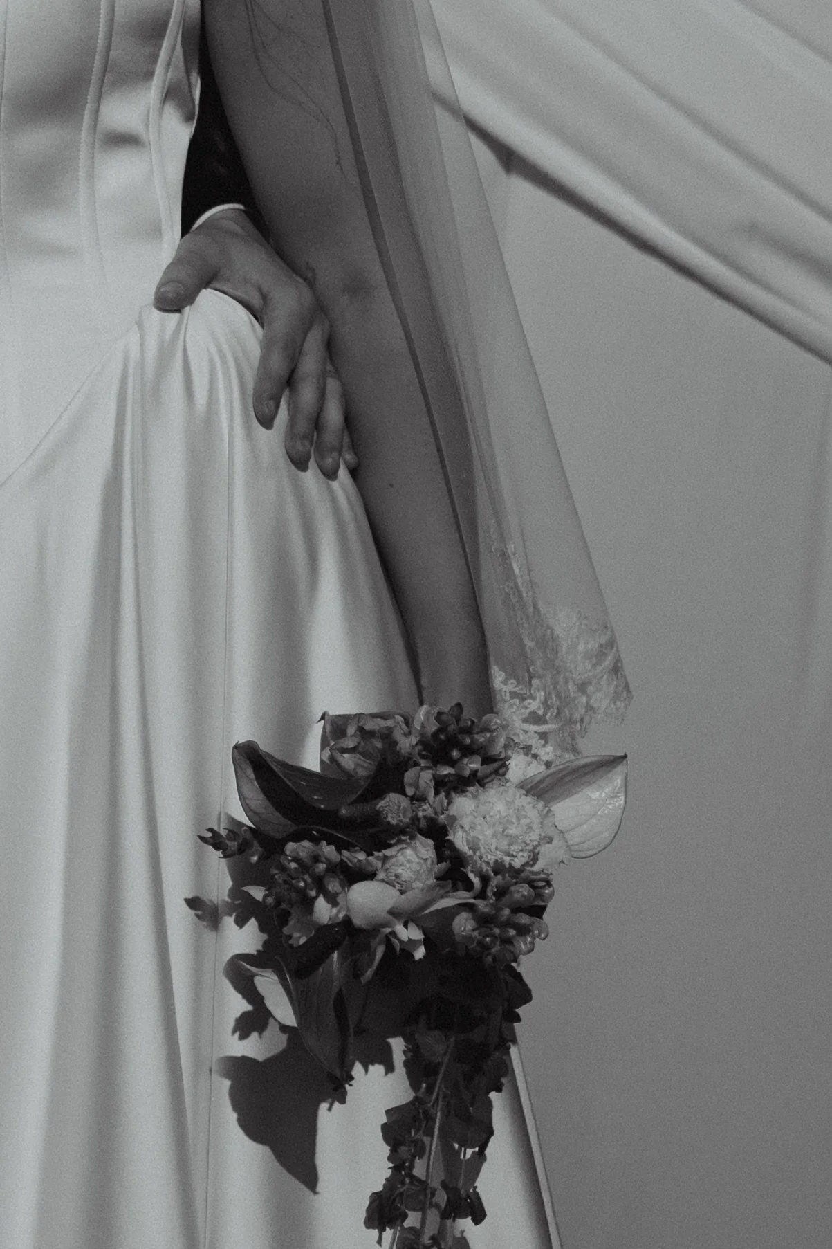 Close-up of a person wearing a white garment, holding a bouquet of flowers, with a curtain in the background.