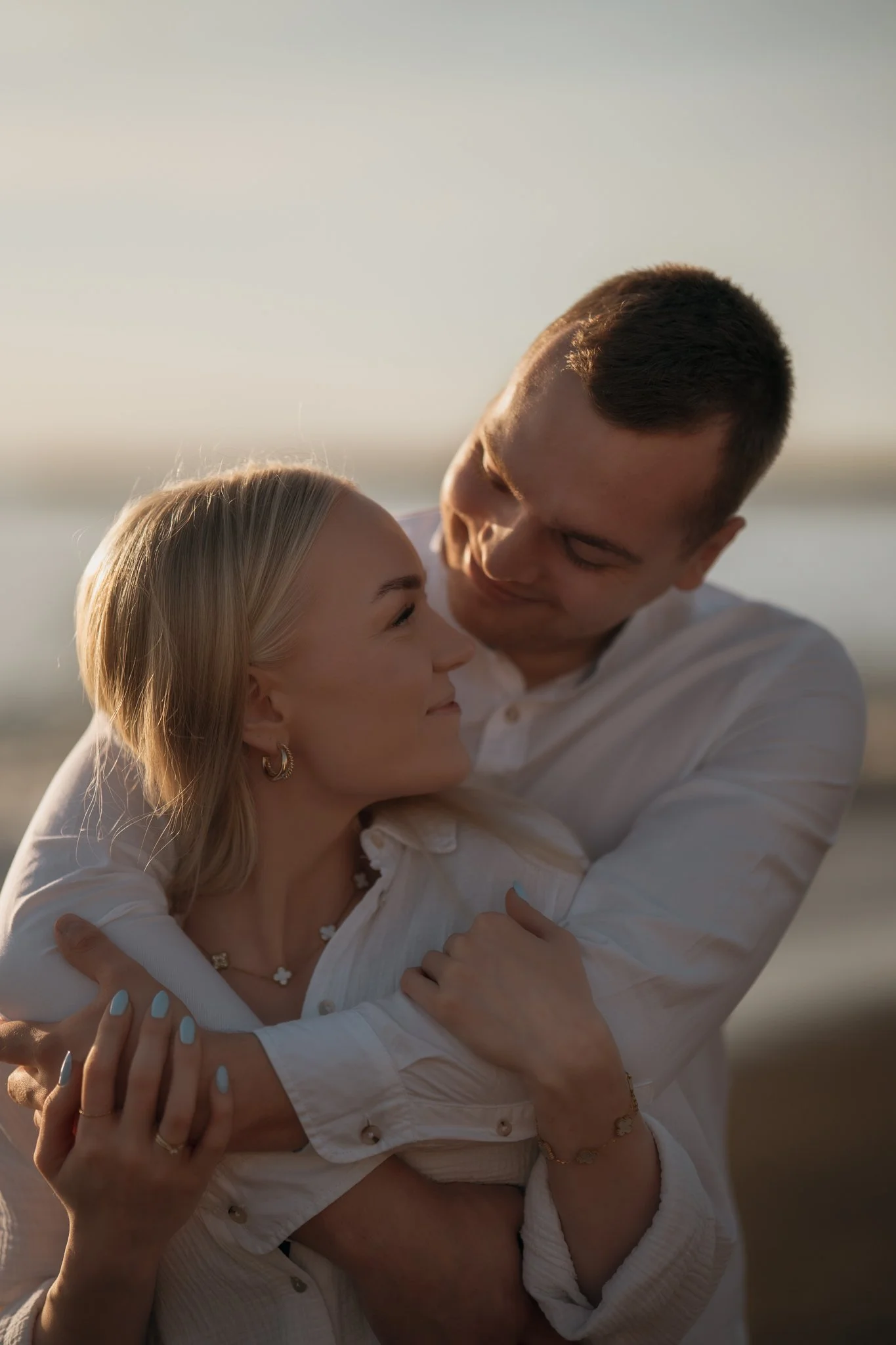 A couple embracing outdoors during sunset, smiling and looking into each other's eyes.
