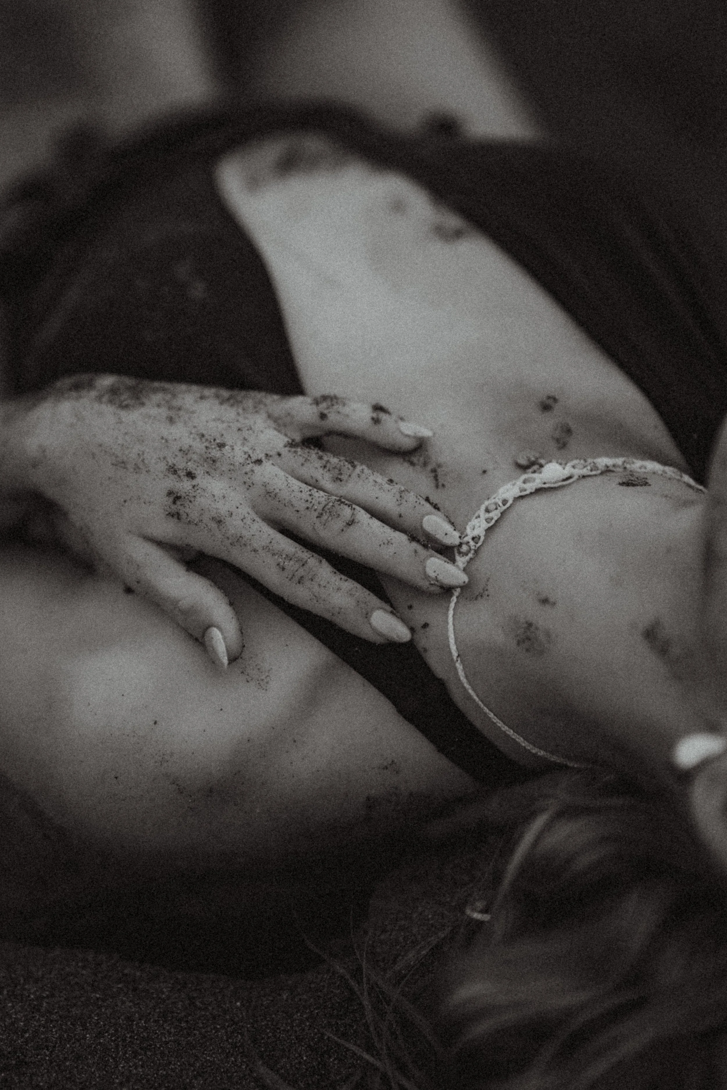 A close-up black and white image of a person's torso with dust or dirt on their hand and arm, wearing a bracelet and a dark top.
