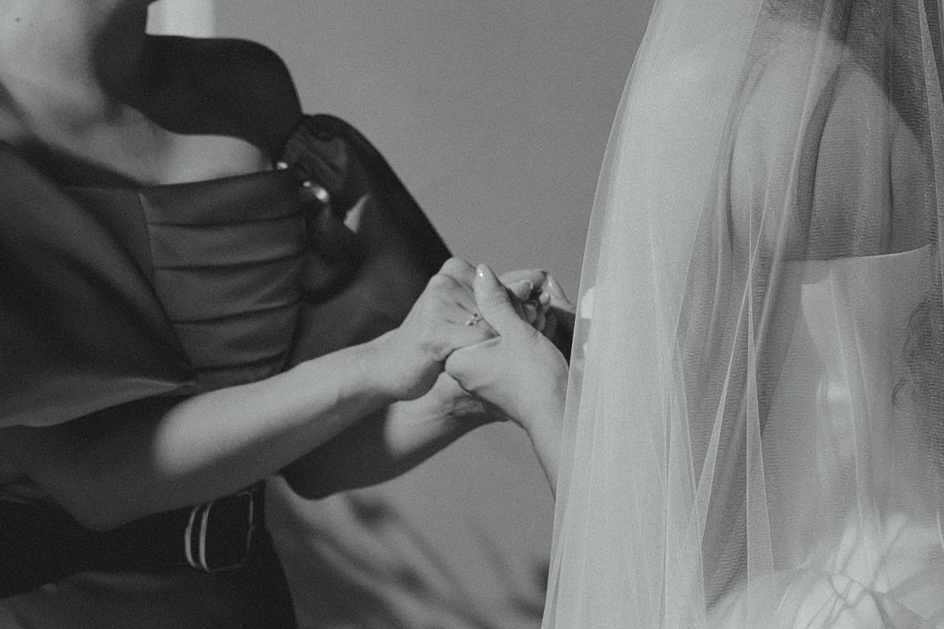 A woman wearing a wedding dress and veil holds hands with a man, who is wearing a suit and tie, during a wedding ceremony.