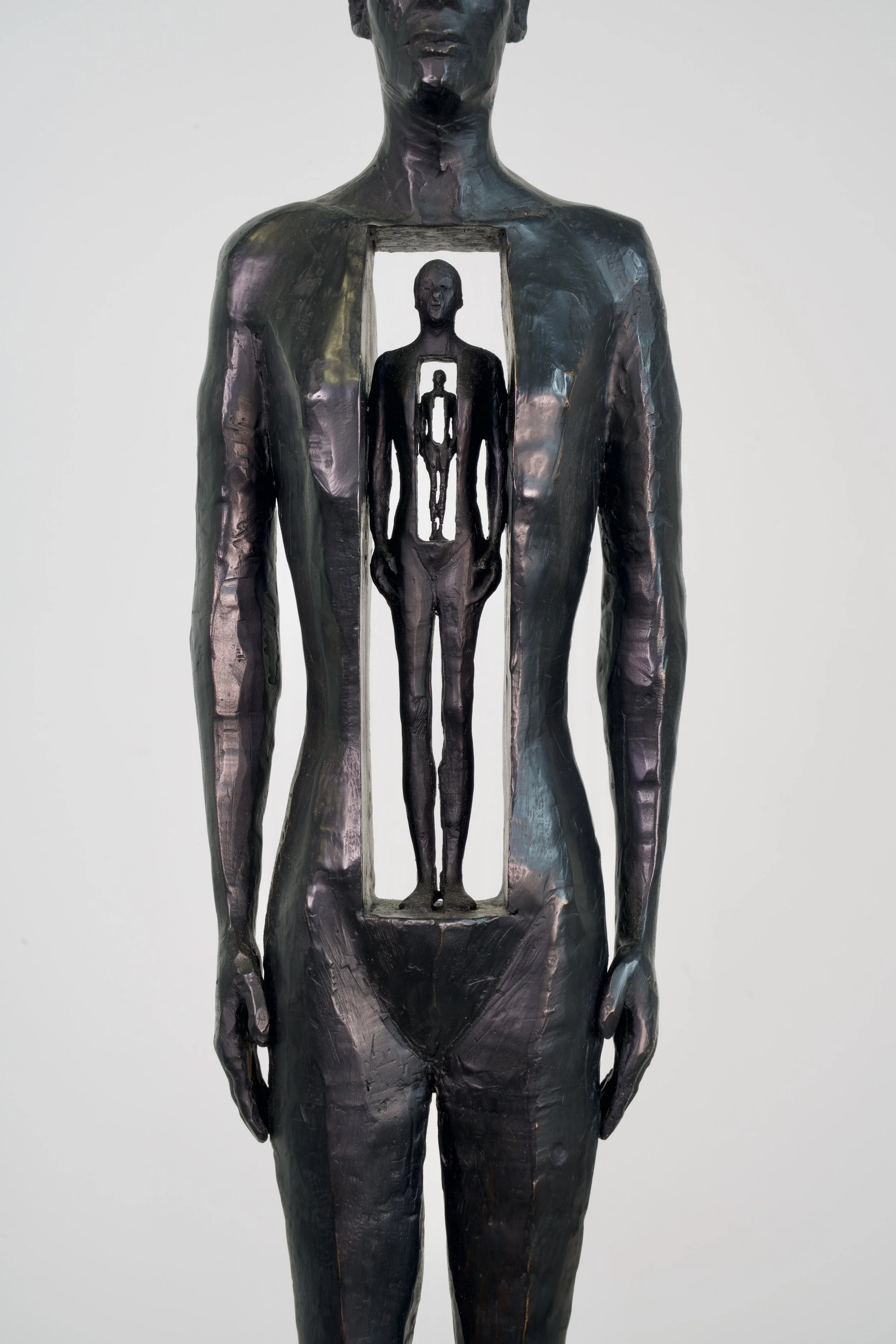 A bronze sculpture of a human figure with an opening in the chest revealing a smaller figure inside, showing a symbolic artistic expression.