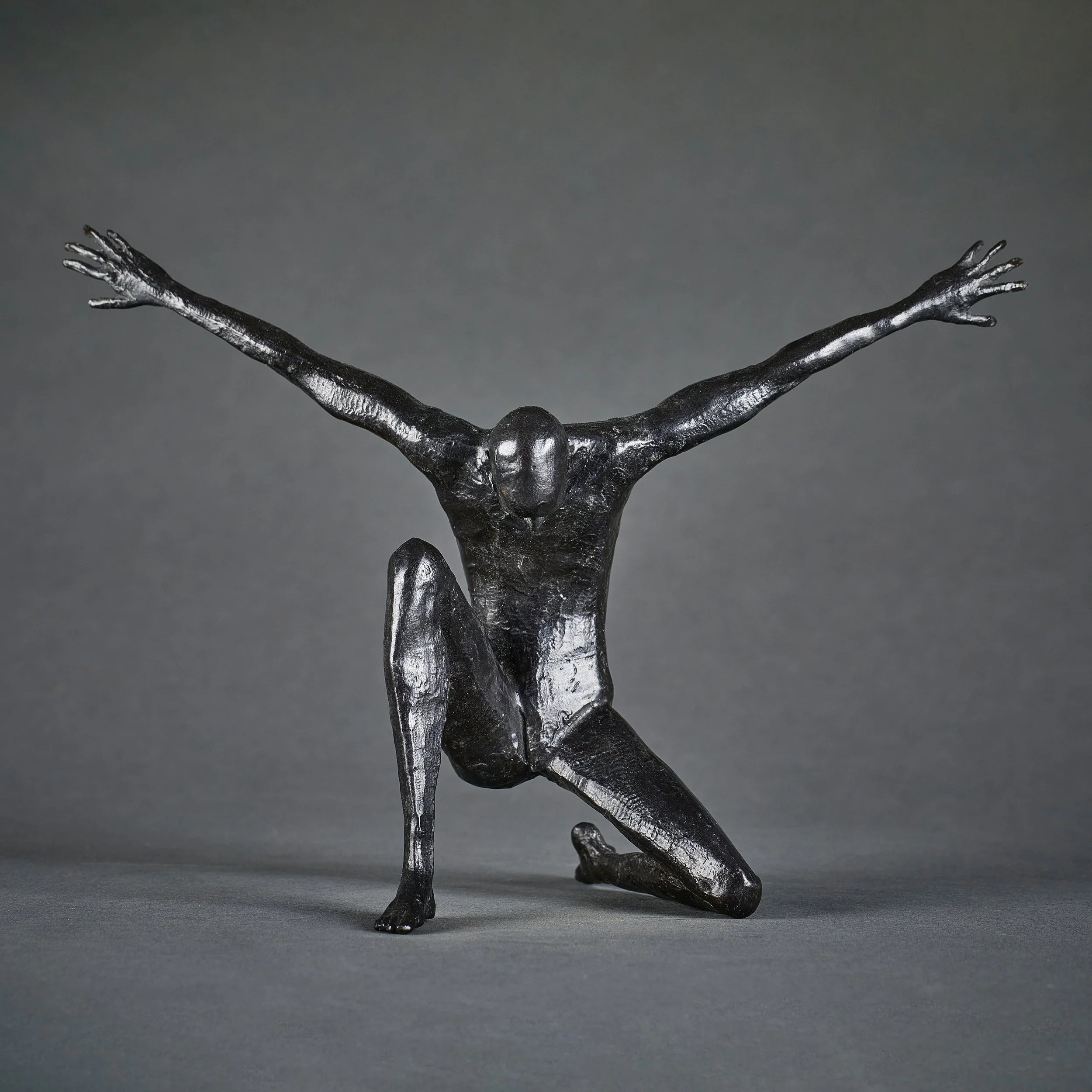 A black metallic sculpture of a person with outstretched arms, positioned against a dark gray background.