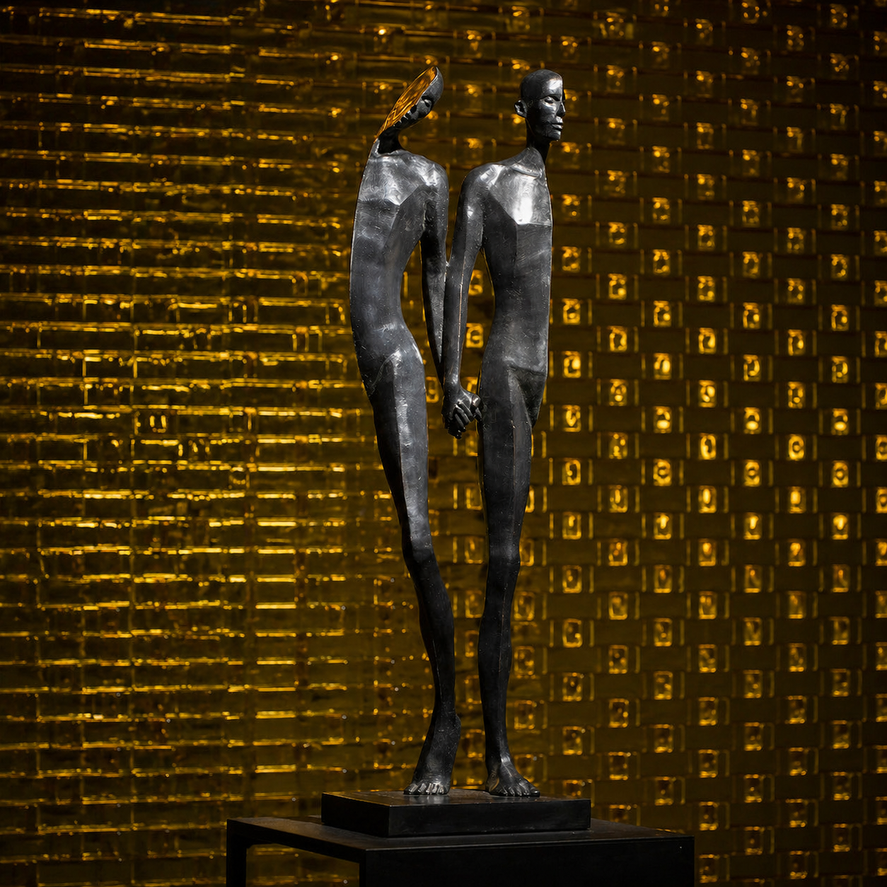 A metal sculpture of two elongated, abstract human figures holding hands, standing on a black pedestal against a gold, textured background.