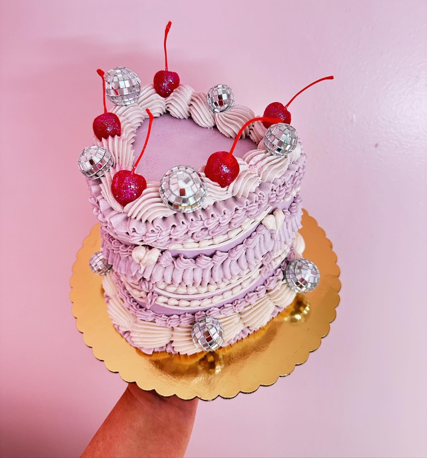 A lavender colored frilly cake with glitter cherries and disco balls! 💜🍒🪩