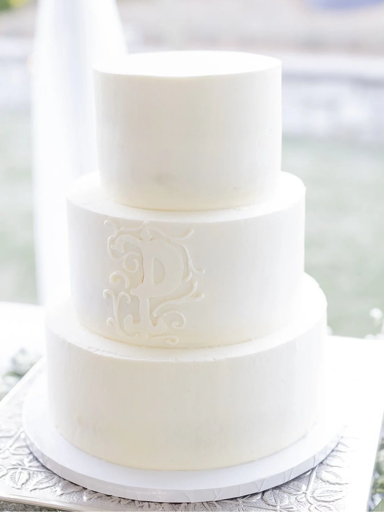 Three-tiered white wedding cake with minimal decoration, featuring an elegant monogram.