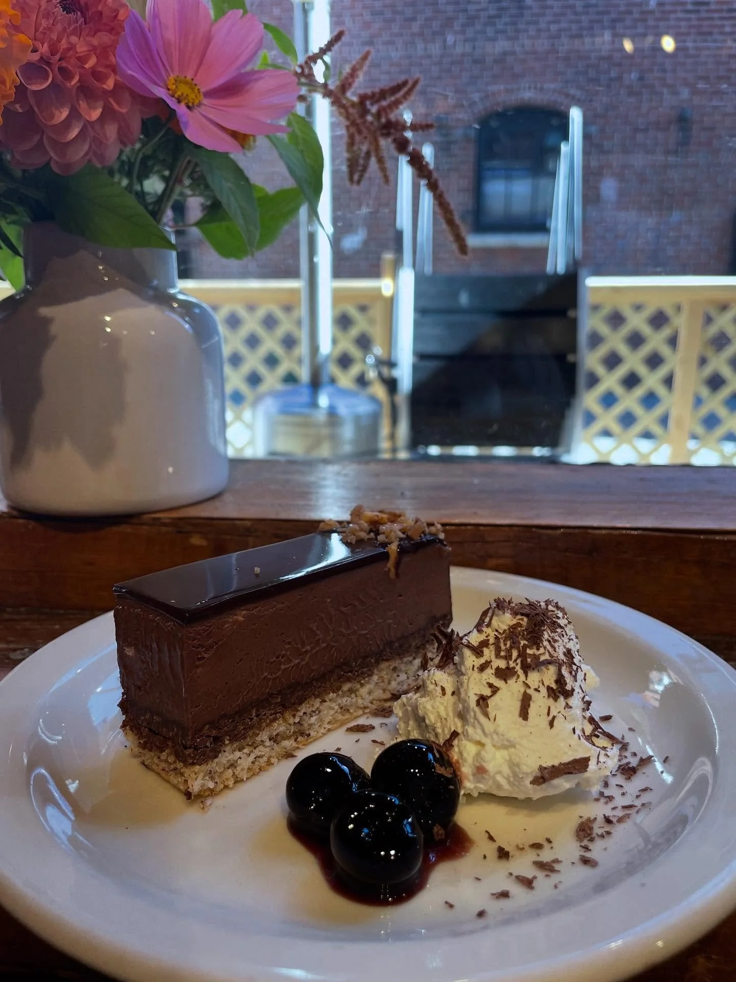 Chocolate Trianon - a French style chocolate mousse layer cake with a hazelnut almond dacquoise, topped with a chocolate mirror glaze and crispy praline, served with luxardo cherries and whipped cream. On special this week.