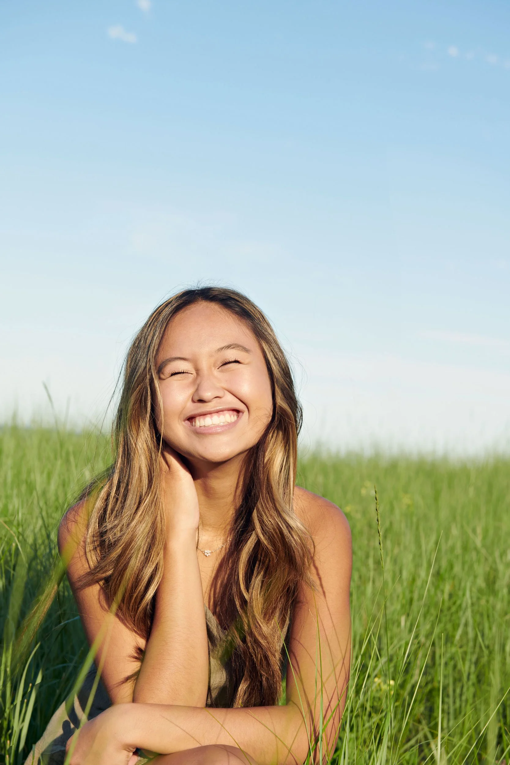 Senior portrait of young woman smiling in a green field under a clear blue sky.
