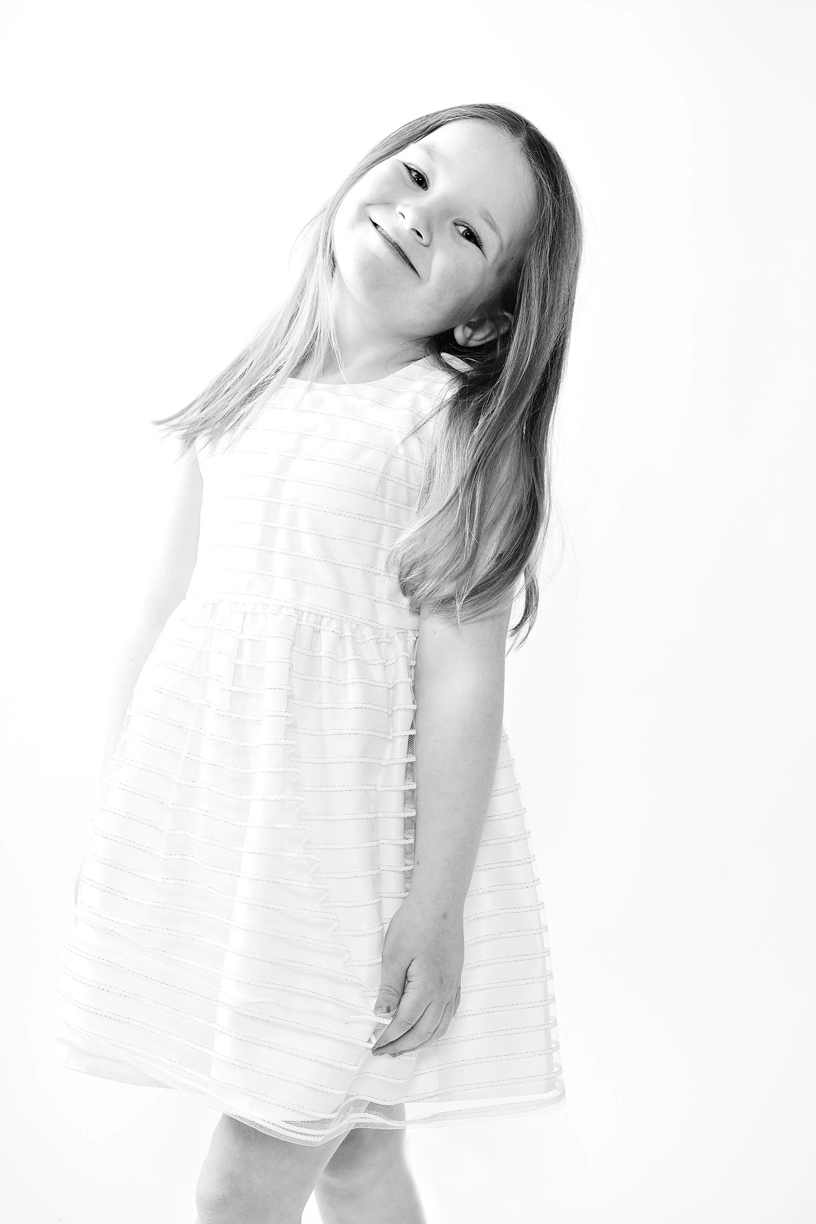 little girl in white dress, smiling with head tilted. black and white image on white background. portsmouth NH