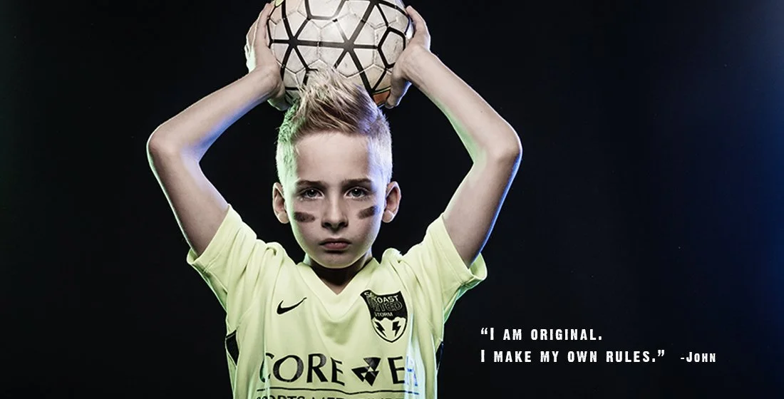 young boy holding a soccer ball over his head against a black background and eye black under his eyes. strong. Portsmouth NH
