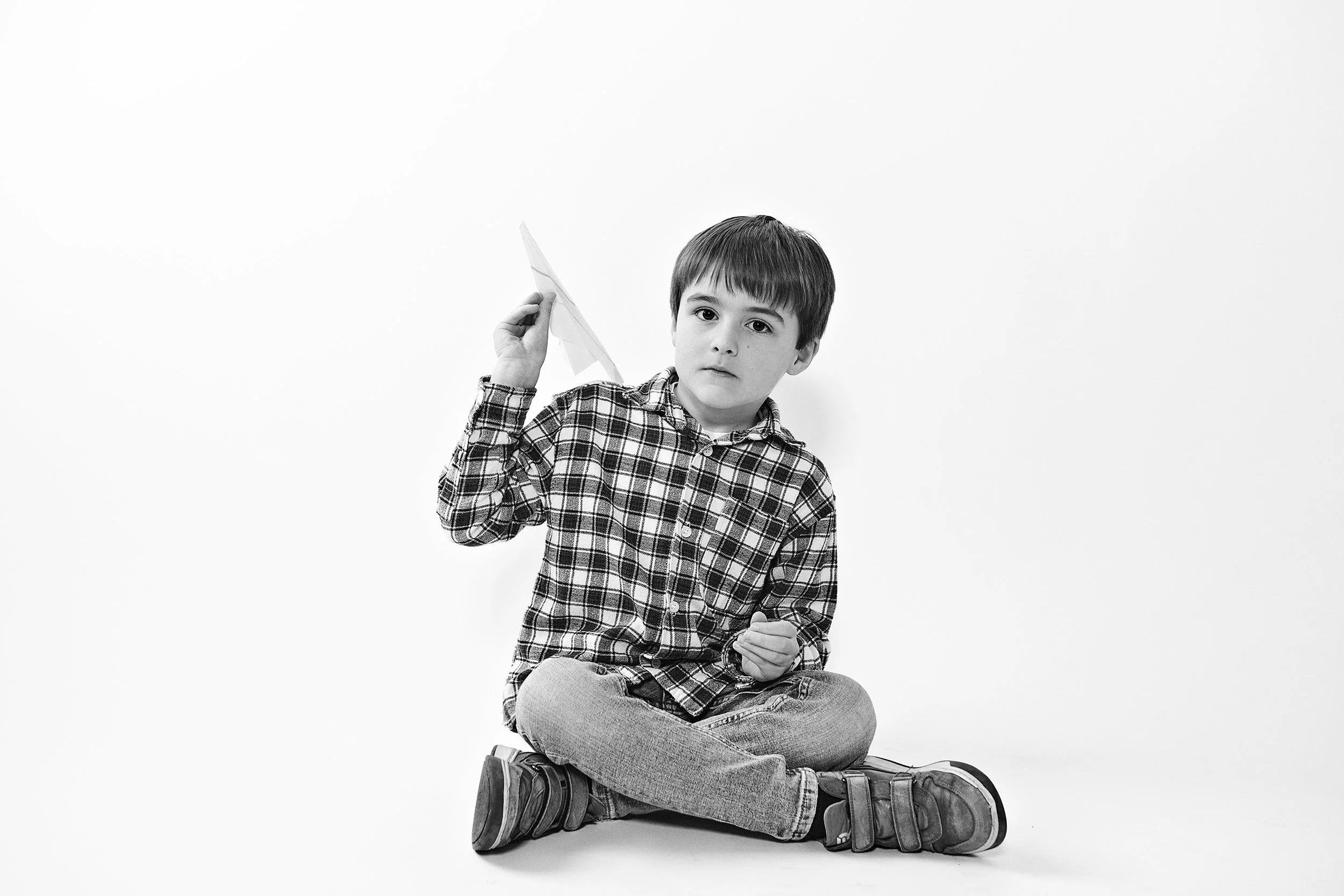little boy sitting crisscross holding a paper airplane. black and white image on white background. portsmouth NH
