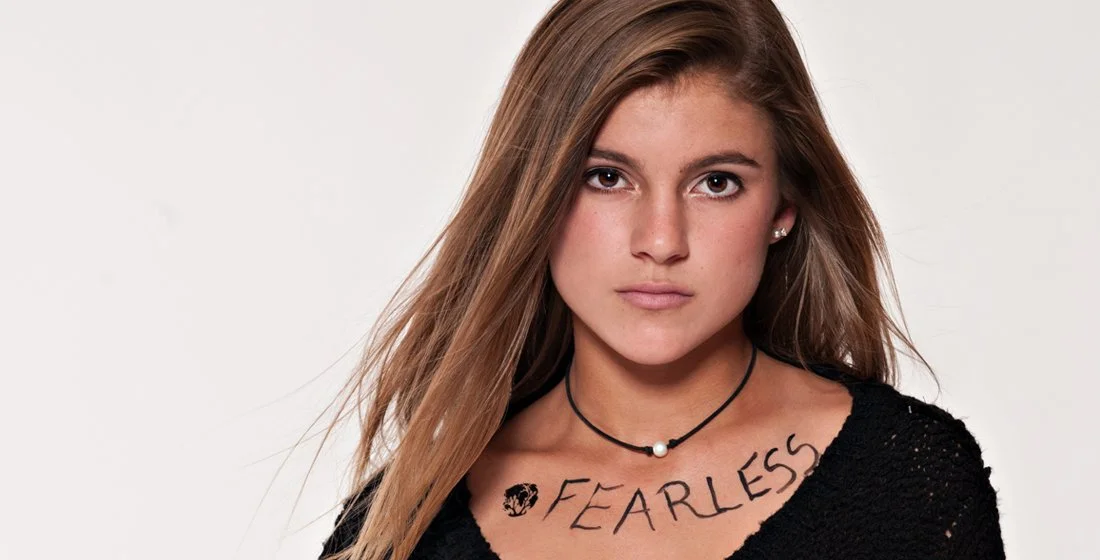 young girl against a white background, brown hair, black shirt with Fearless witten on her 