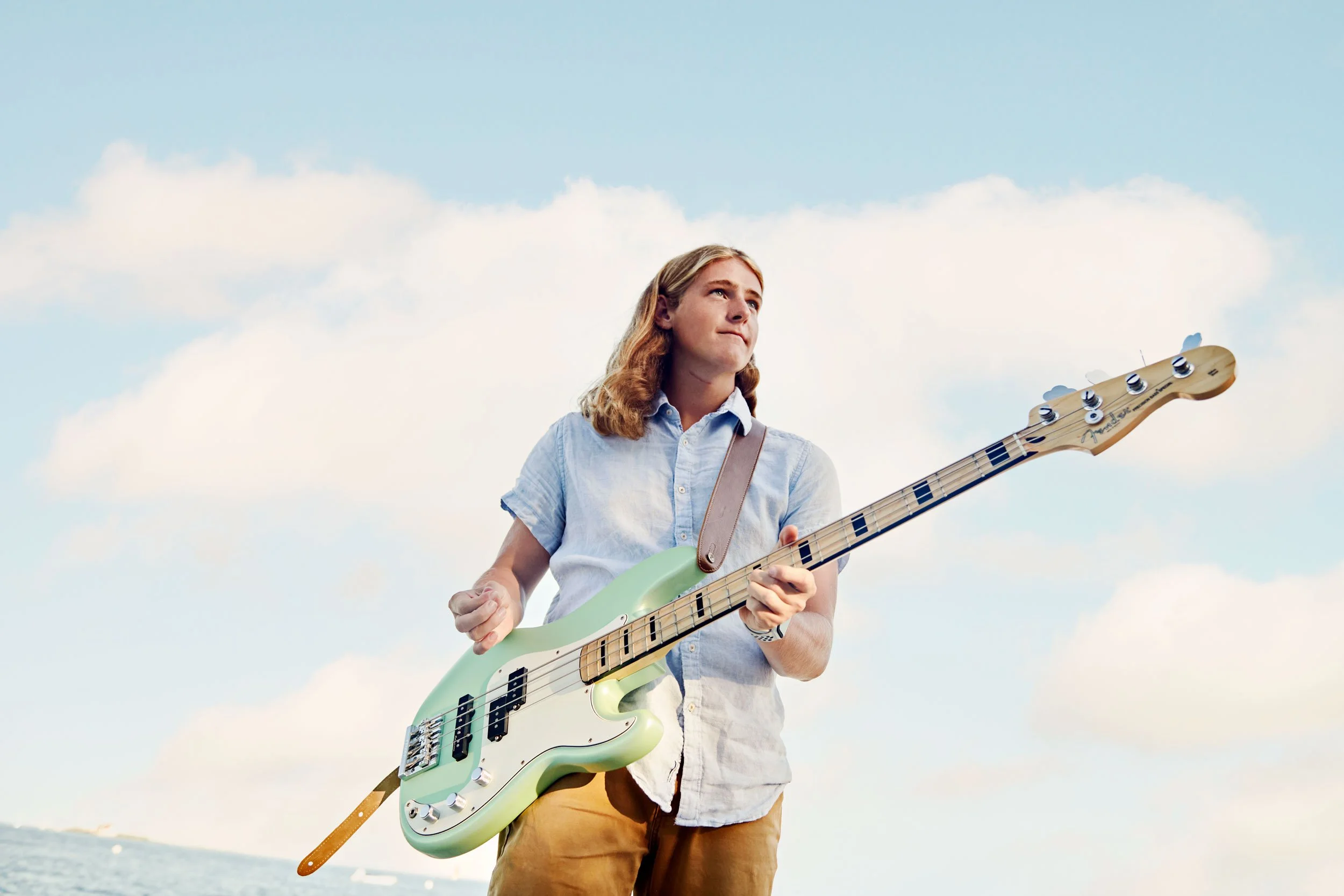 Senior portrait of a young man playing a green electric bass guitar outdoors with a blue sky backdrop.