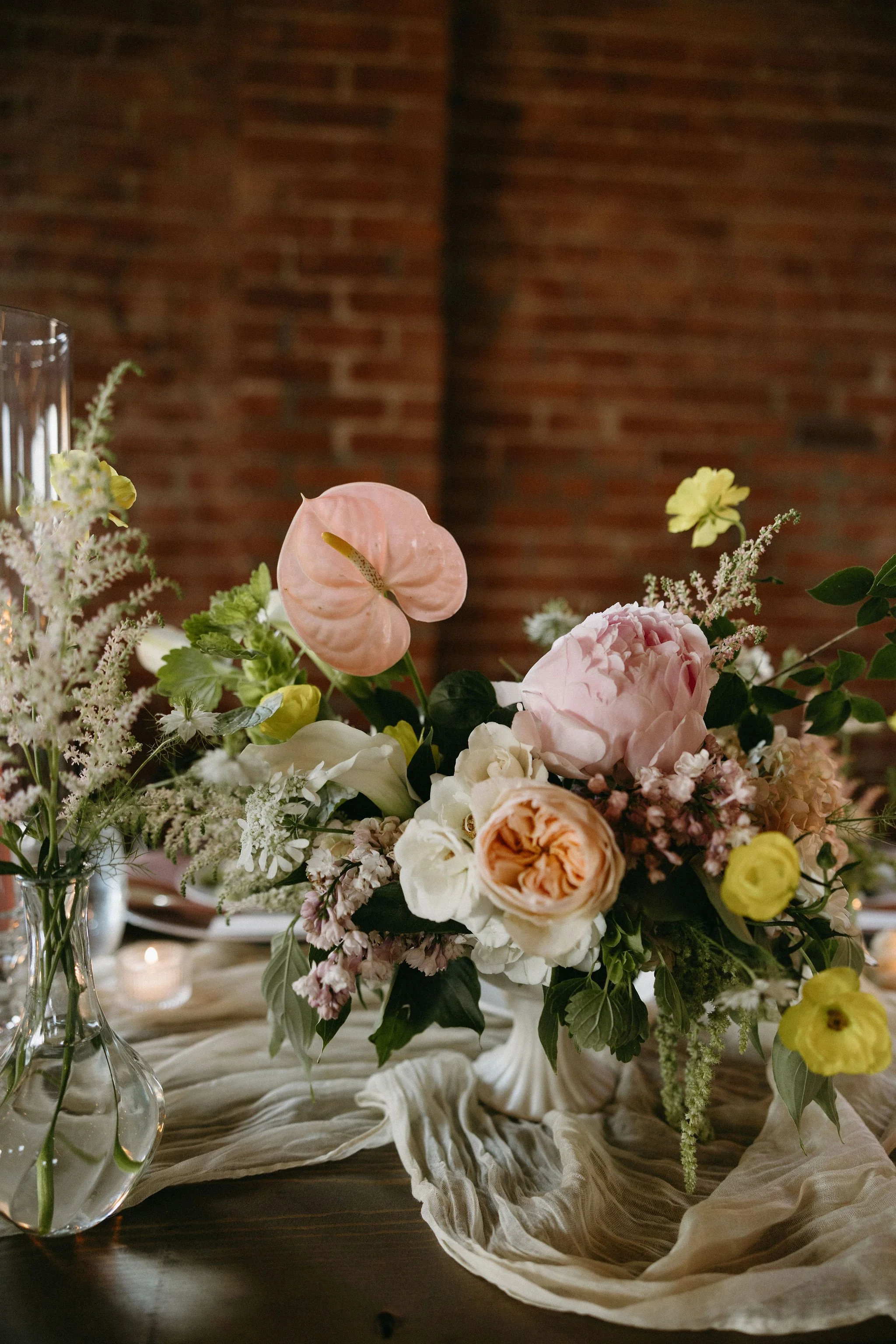 modern spring garden wedding warm color palette yellow peach green the cottage rose kansas city florist crossroads powell garden reception hanging greenery bud vases taper candles anthurium flower arrangement centerpiece head table decor peonies