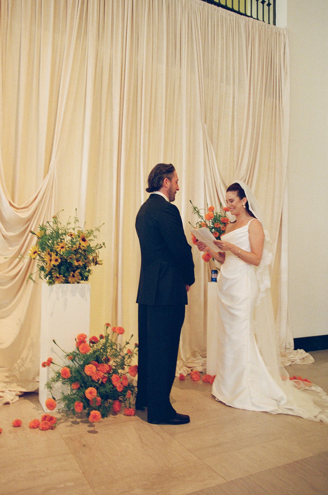 Modern september wedding ceremony ivory draped fabric orange and yellow color palette floral pedestals marigolds library wedding ceremony bride and groom  the cottage rose kansas city wedding florist crossroads hotel kansas city wedding