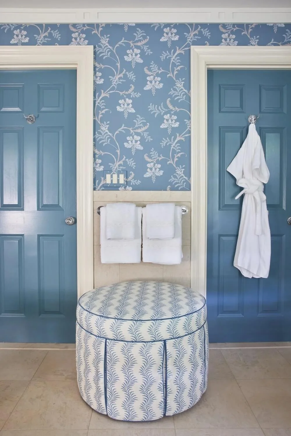 New England luxury bathroom with blue-green doors, fern fabric ottoman, and classic wallpaper